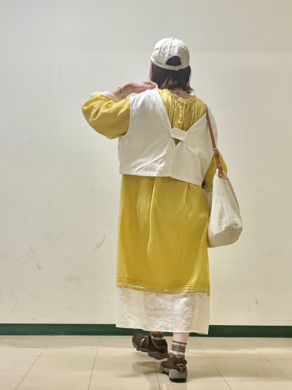 ホワイト系のベスト、イエロー系のワンピース、ベージュ系のキャップを着用したレディースの夏コーディネートの2枚目の写真