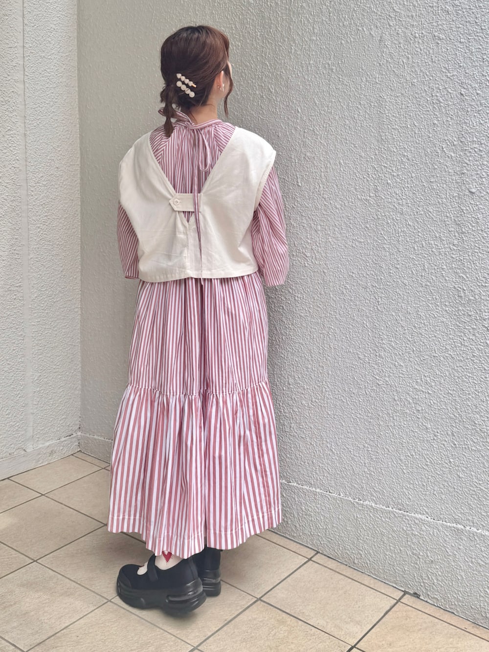 ホワイト系のベスト、ピンク系のワンピース、ブラック系のスニーカーを着用したレディースの春コーディネートの3枚目の写真