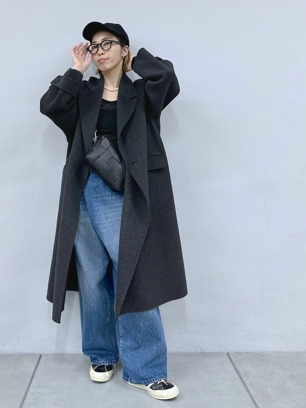 ブラック系のショルダーバッグ、ブルー系のデニムパンツ、グレー系のチェスターコートを着用したレディースの秋コーディネートの2枚目の写真