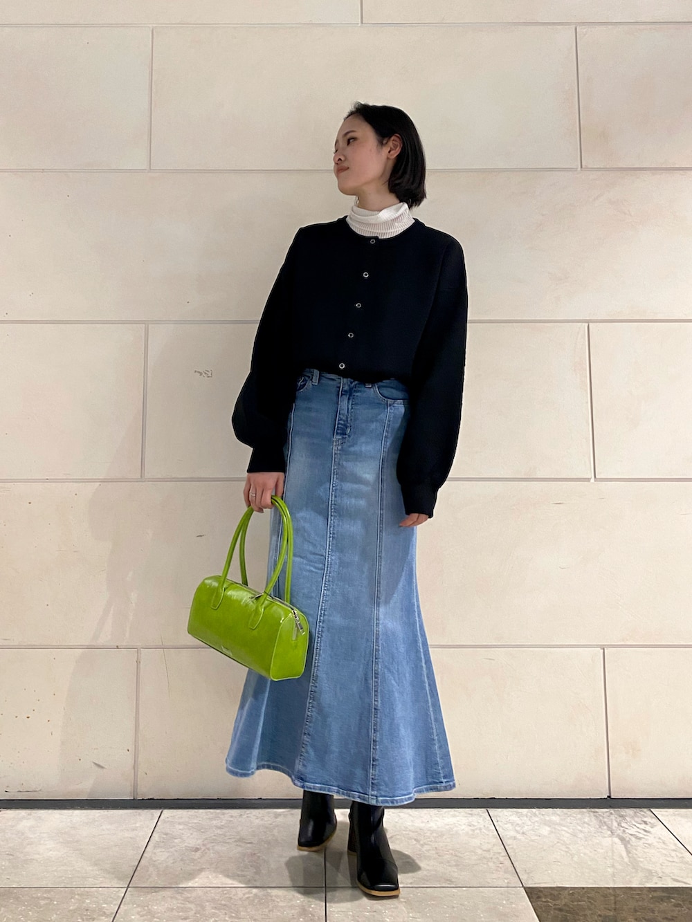 ブラック系のカーディガン/ボレロ、ブルー系のデニムスカート、グリーン系のボストンバッグを着用したレディースの冬コーディネートの2枚目の写真