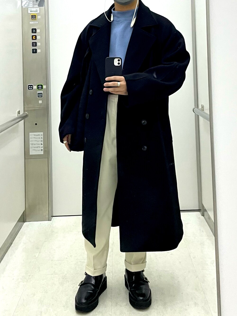 ブラック系のチェスターコート、ブルー系のニット/セーター、ホワイト系のスラックスを着用したメンズの冬コーディネートの2枚目の写真