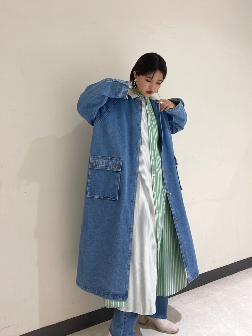 グリーン系のシャツワンピース、ブルー系のベスト、ブルー系のデニムパンツを着用したレディースの冬コーディネートの2枚目の写真