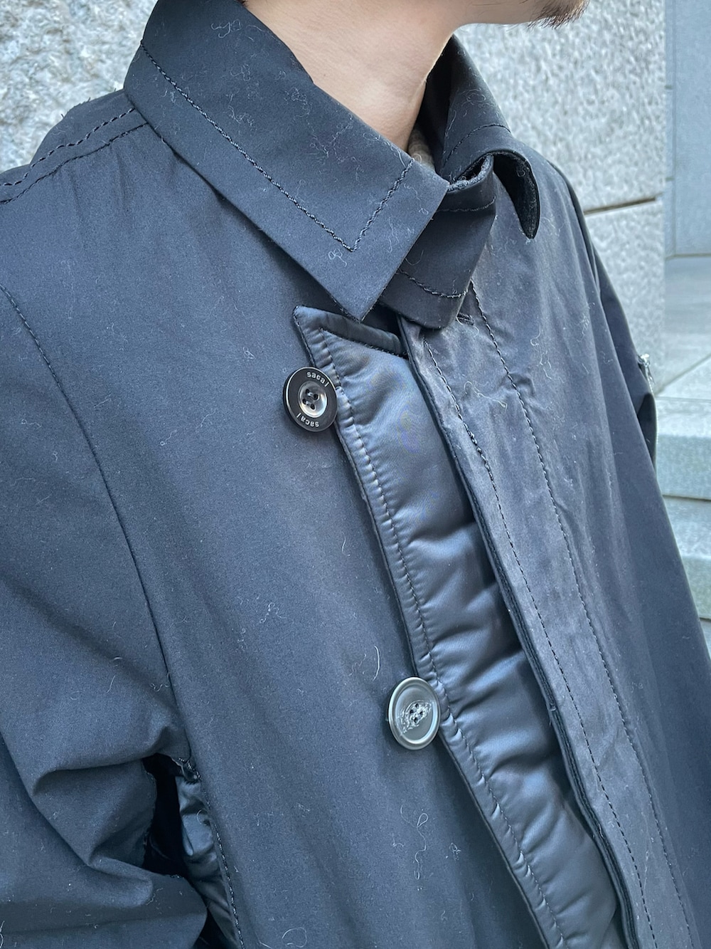 ブラック系のステンカラーコート、ブラック系のデニムパンツ、ブルー系のスニーカーを着用したメンズの冬コーディネートの4枚目の写真