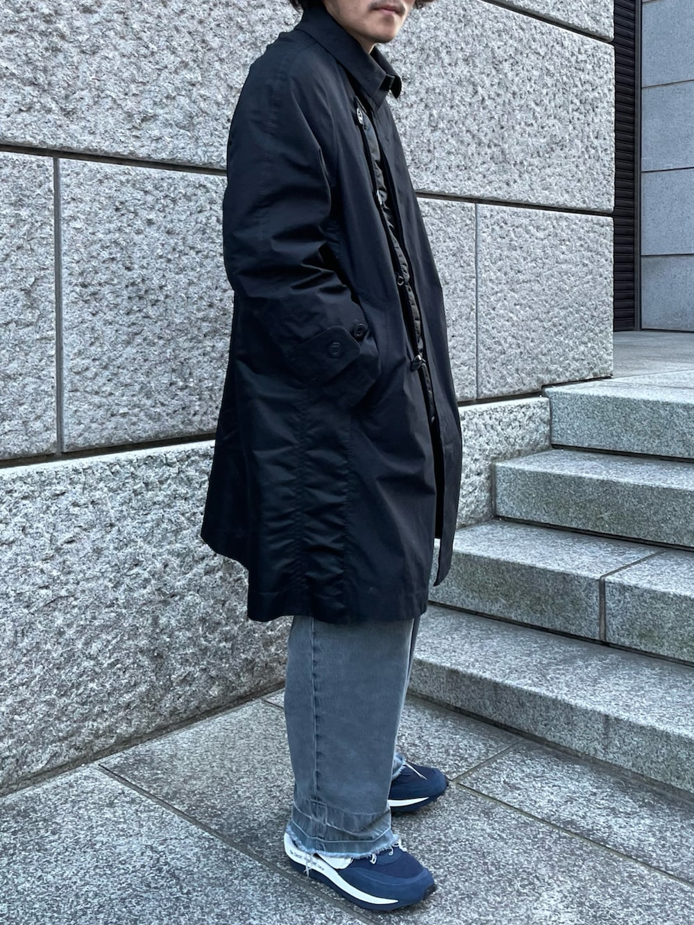 ブラック系のステンカラーコート、ブラック系のデニムパンツ、ブルー系のスニーカーを着用したメンズの冬コーディネートの3枚目の写真