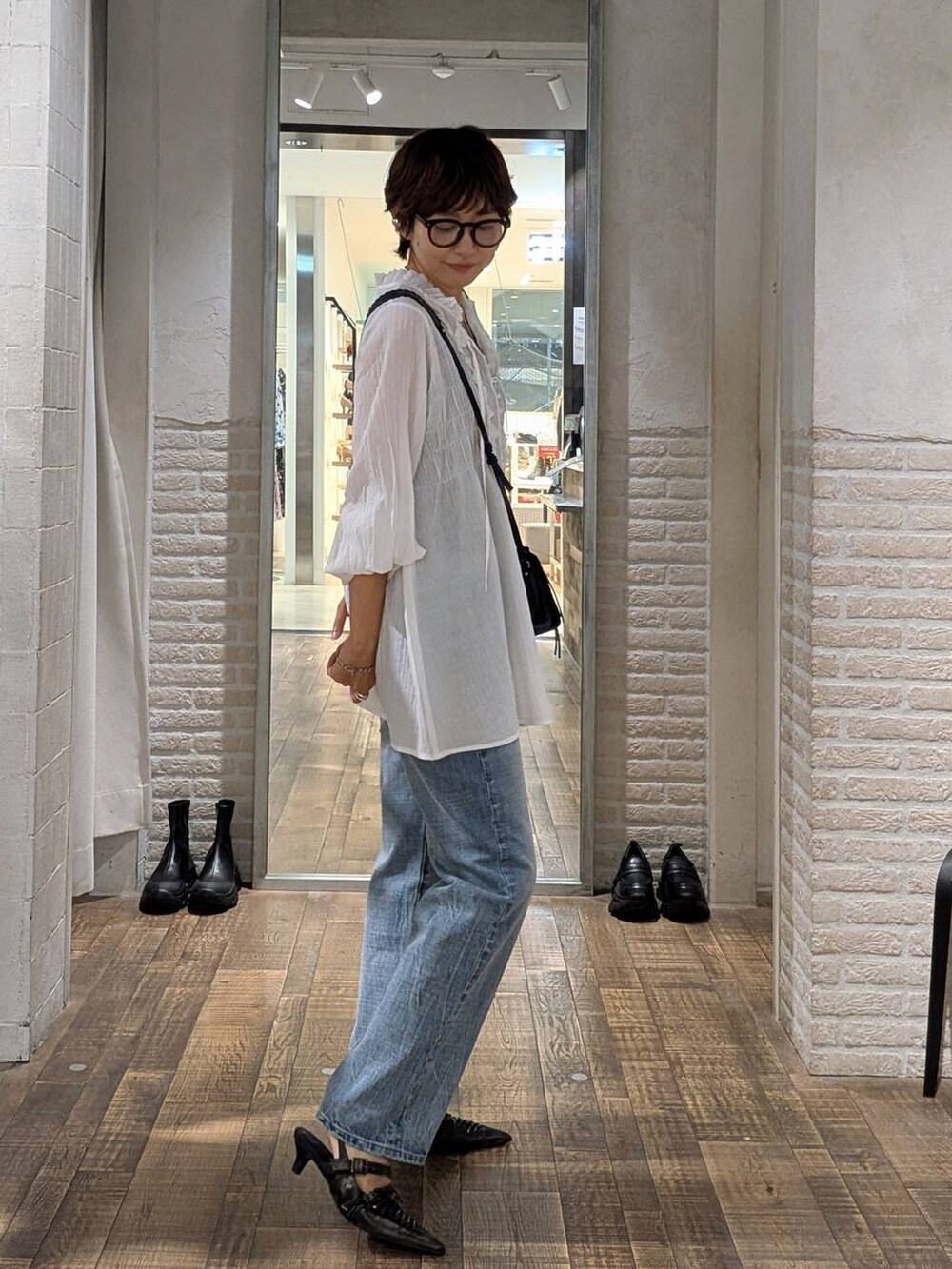 ブラック系のパンプス、ブルー系のデニムパンツ、ホワイト系のチュニックを着用したレディースの秋コーディネートの2枚目の写真