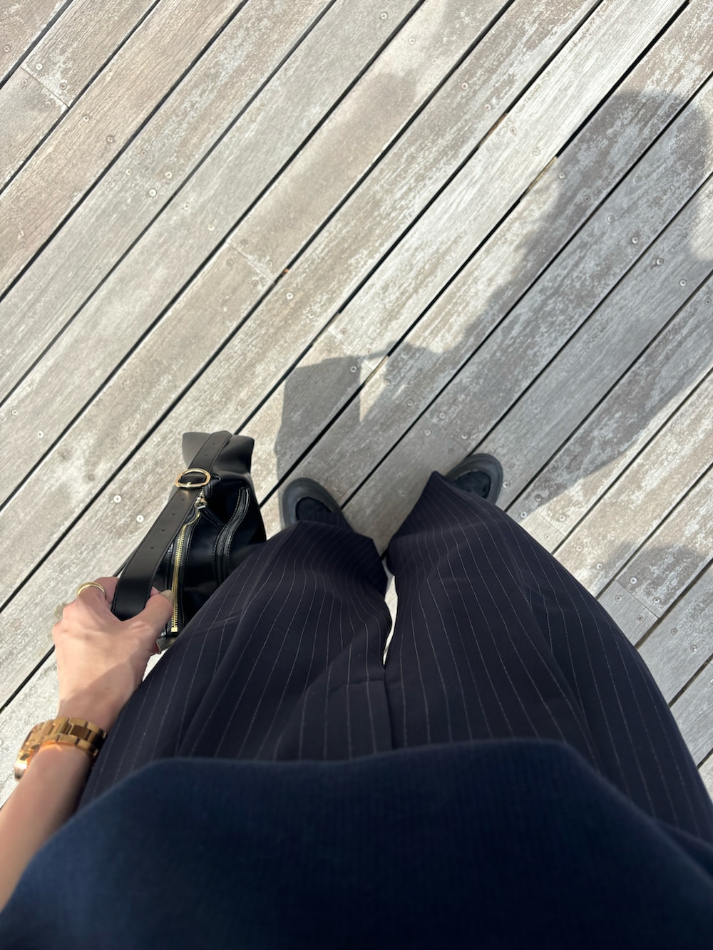 ブラック系のハンドバッグ、ブルー系のパンツ、ブラック系のスニーカーを着用したレディースの夏コーディネートの2枚目の写真