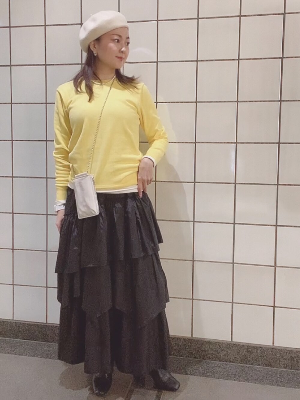 イエロー系のニット/セーター、ブラック系のスカート、ホワイト系のTシャツ/カットソーを着用したレディースの春コーディネートの2枚目の写真