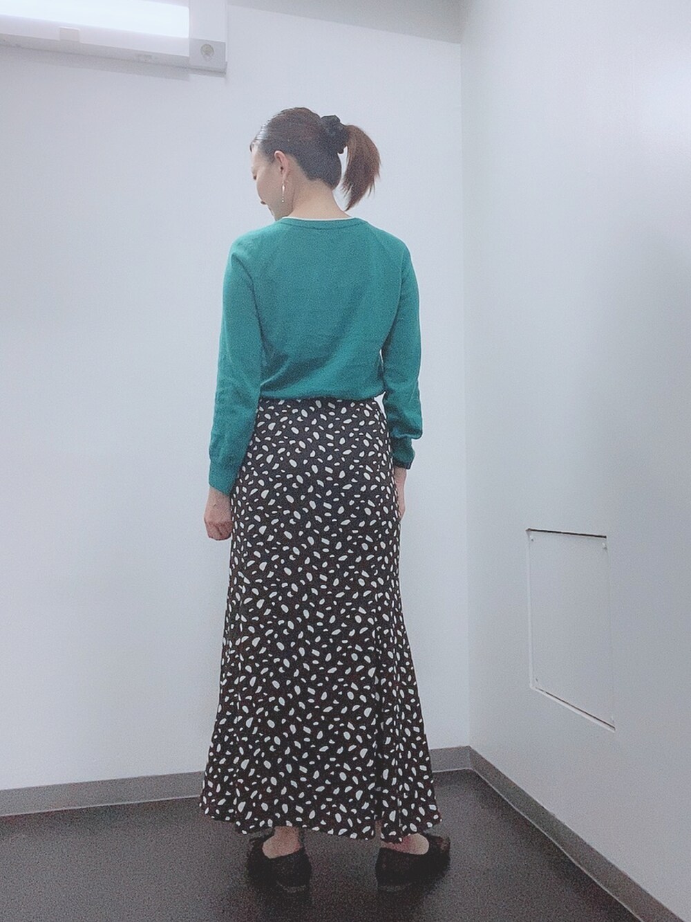 グリーン系のニット/セーター、ブラック系のスカート、ブラック系のレインシューズを着用したレディースの春コーディネートの3枚目の写真