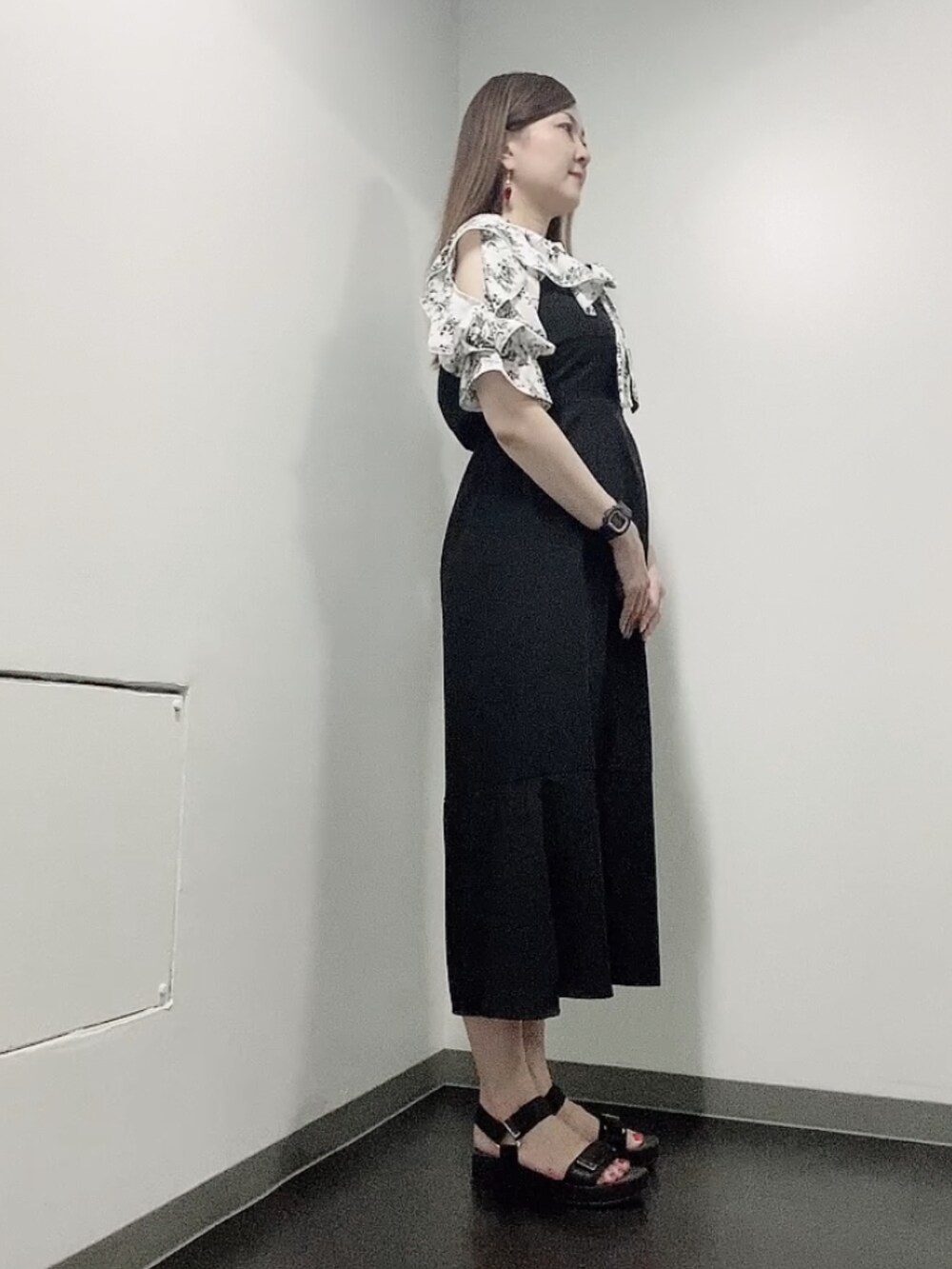 ブラック系のワンピース、ブラック系のサンダル、ゴールド系のピアス（両耳用）を着用したレディースの夏コーディネートの2枚目の写真