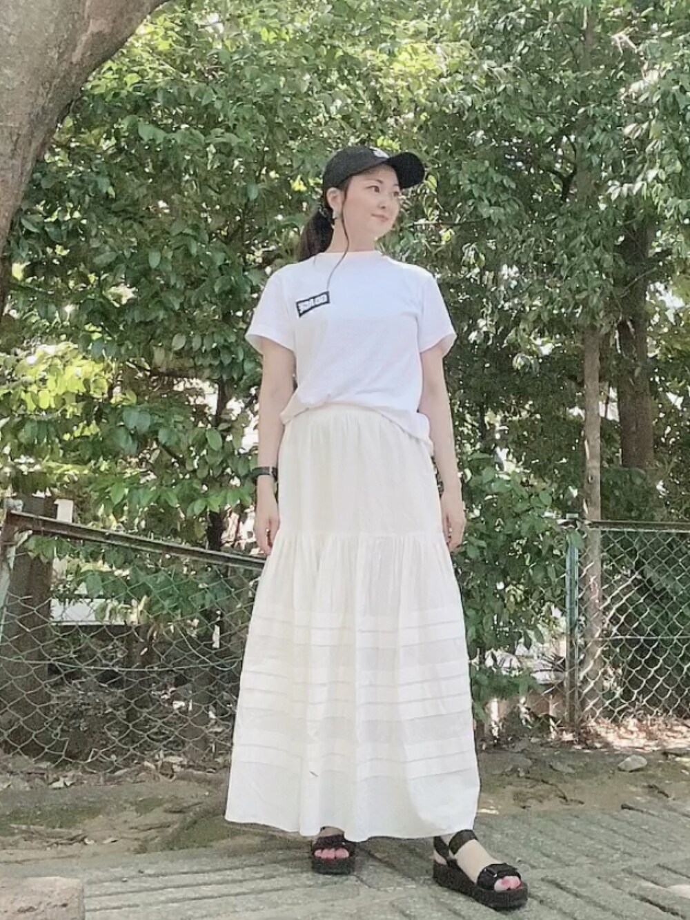 ホワイト系のTシャツ/カットソー、ホワイト系のスカート、ブラック系のサンダルを着用したレディースの夏コーディネートの2枚目の写真