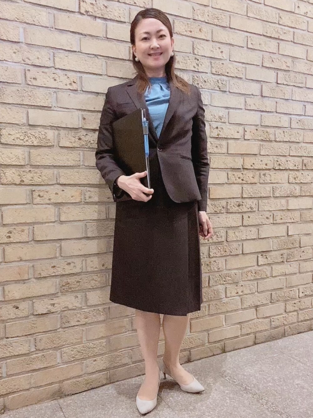 ブラウン系のスーツセット、グレー系のパンプス、ブルー系のシャツ/ブラウスを着用したレディースの秋コーディネートの2枚目の写真