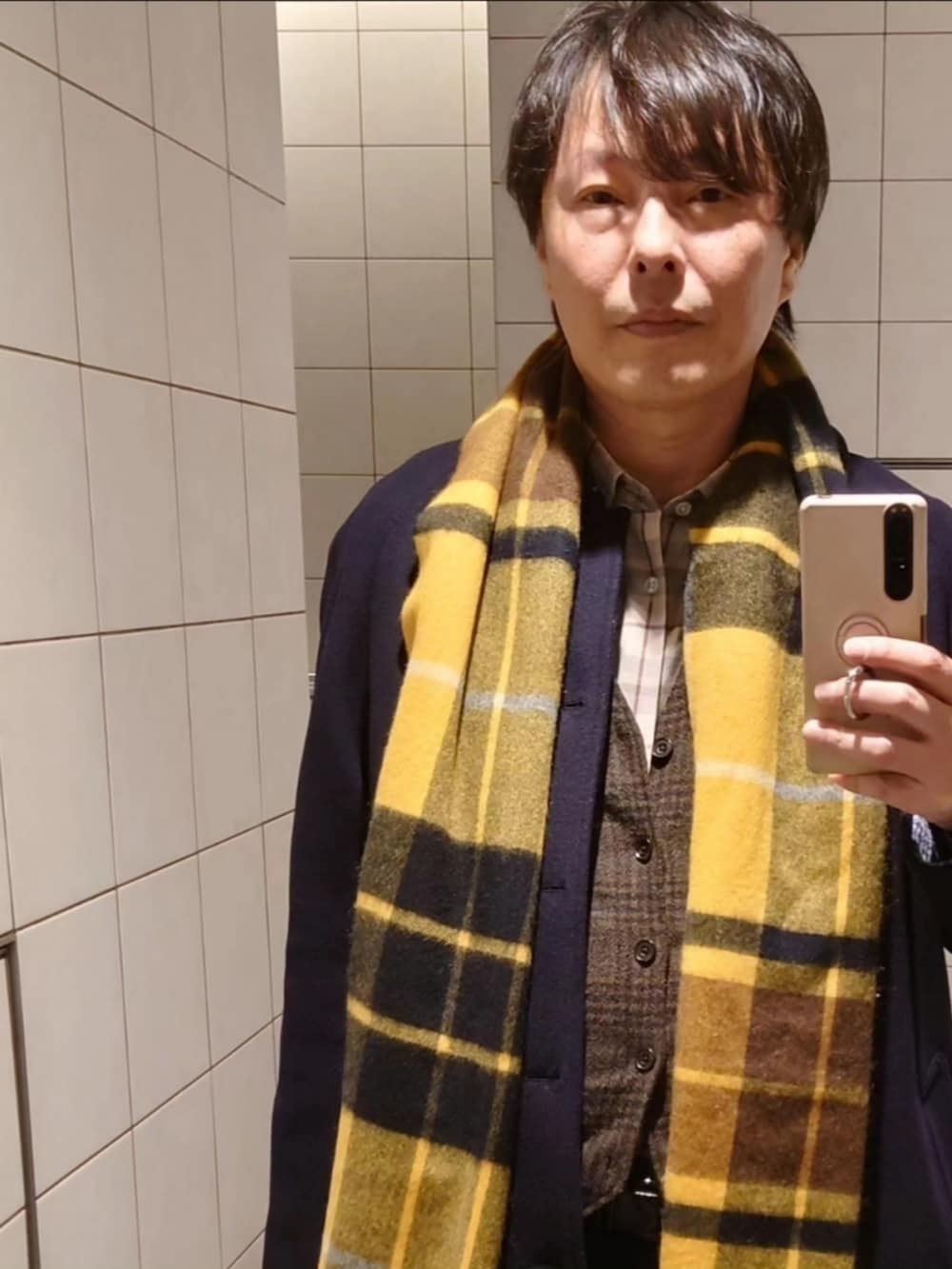 ブラック系のステンカラーコート、ブラウン系のブーツ、ブルー系のテーラードジャケットを着用したメンズの冬コーディネートの2枚目の写真