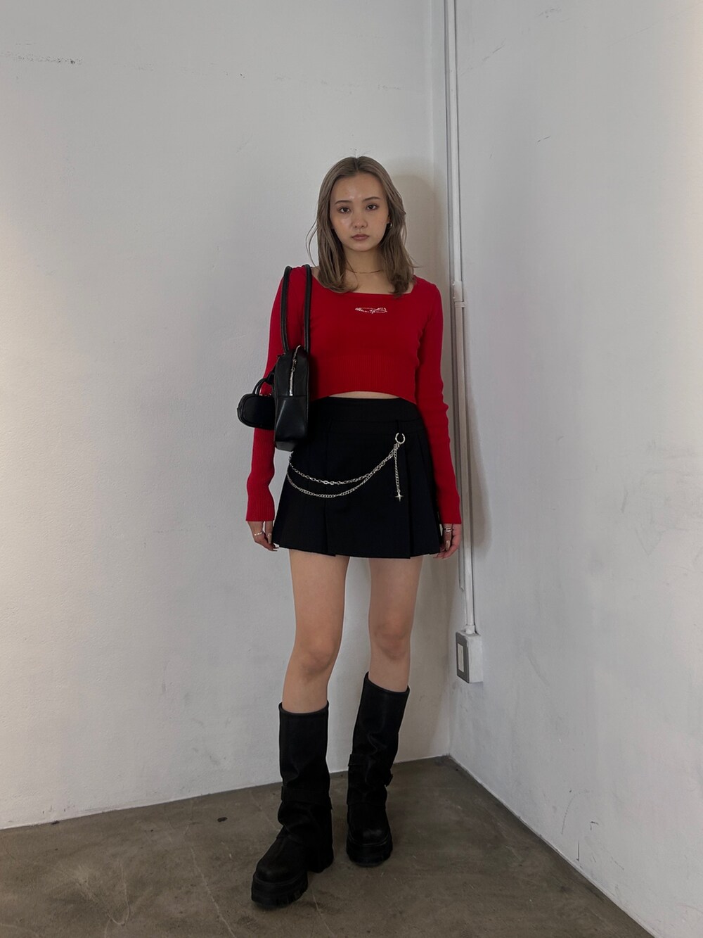 レッド系のニット/セーター、ブラック系のスカート、ブラック系のブーツを着用したレディースの冬コーディネートの2枚目の写真