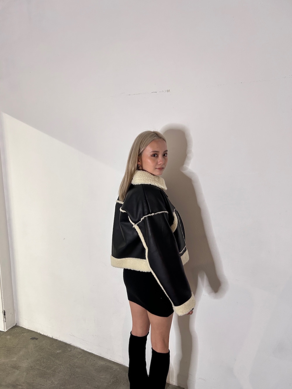 ブラック系のブルゾン、ブラック系のブーツ、ブラック系のワンピースを着用したレディースの冬コーディネートの2枚目の写真