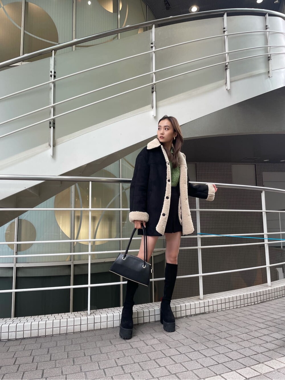 グリーン系のニット/セーター、ブラック系のスカート、ブラック系のムートンコートを着用したレディースの冬コーディネートの4枚目の写真