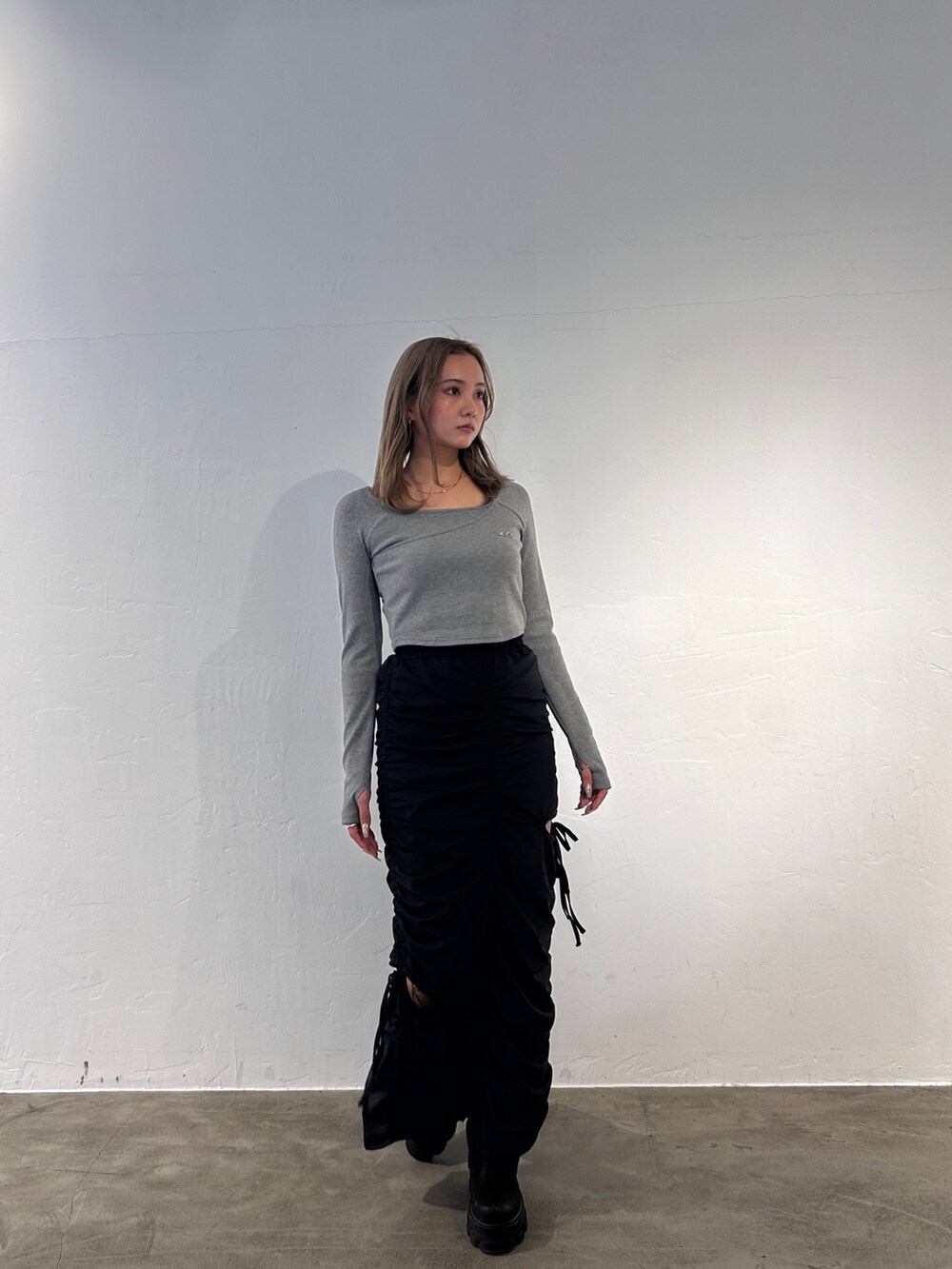 グレー系のTシャツ/カットソー、ブラック系のスカート、ブラック系のブーツを着用したレディースの冬コーディネートの2枚目の写真