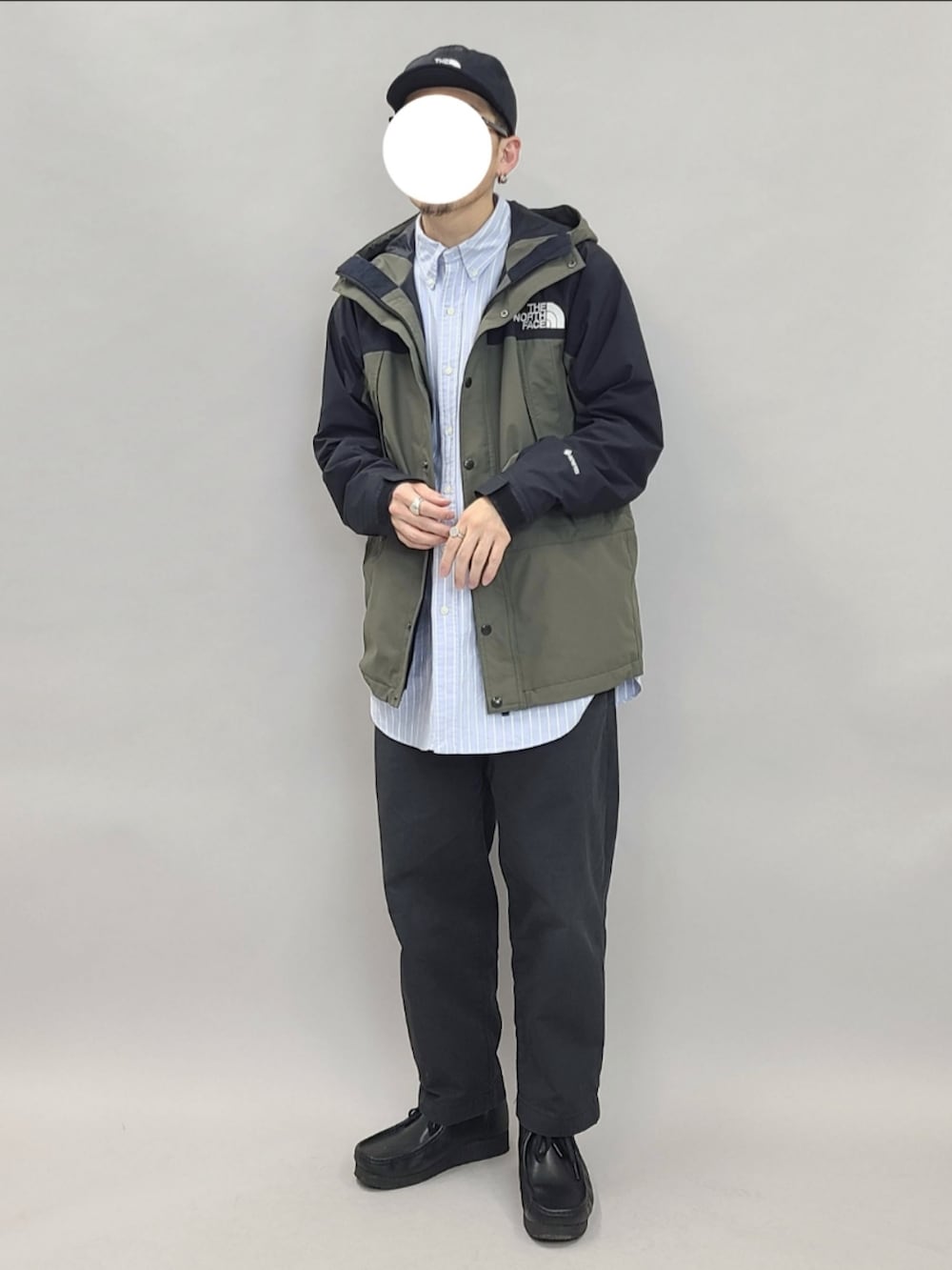 グリーン系のマウンテンパーカー、ブラック系のブーツ、ブラック系のキャップを着用したメンズの春コーディネートの2枚目の写真