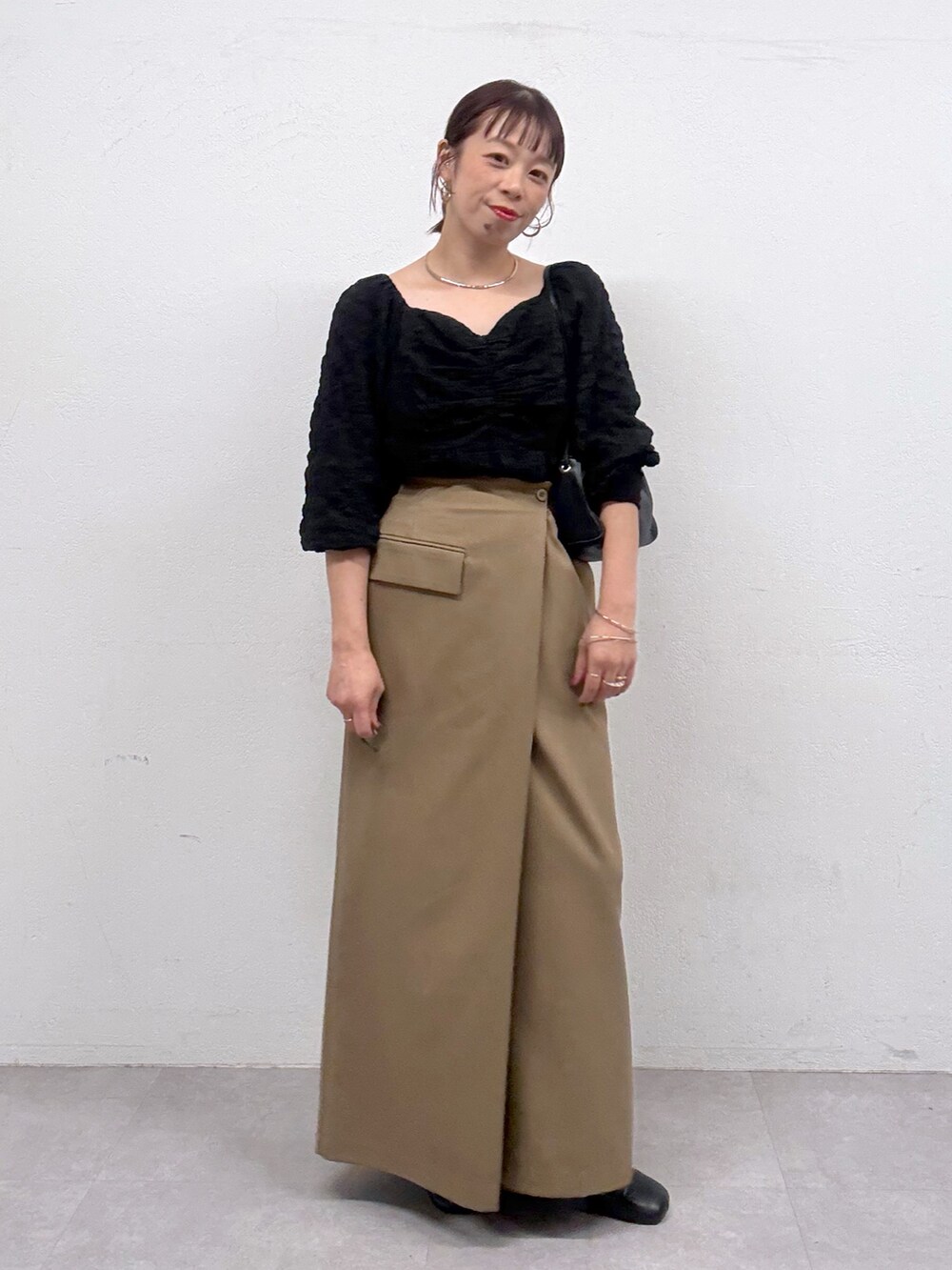 ベージュ系のスカート、ブラック系のシャツ/ブラウス、ブラック系のブーツを着用したレディースの秋コーディネートの2枚目の写真