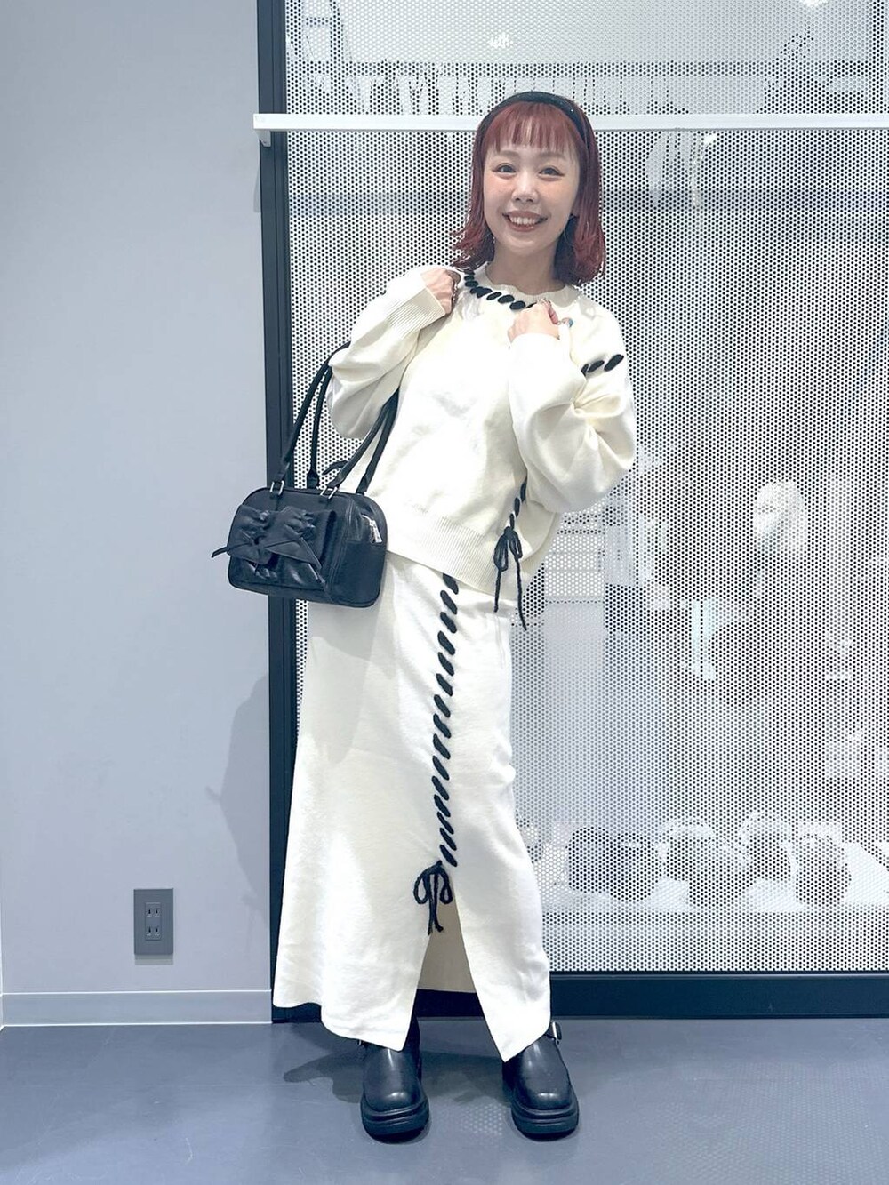 ブラック系のブーツ、ブラック系のハンドバッグ、ベージュ系のスカートを着用したレディースの秋コーディネートの2枚目の写真