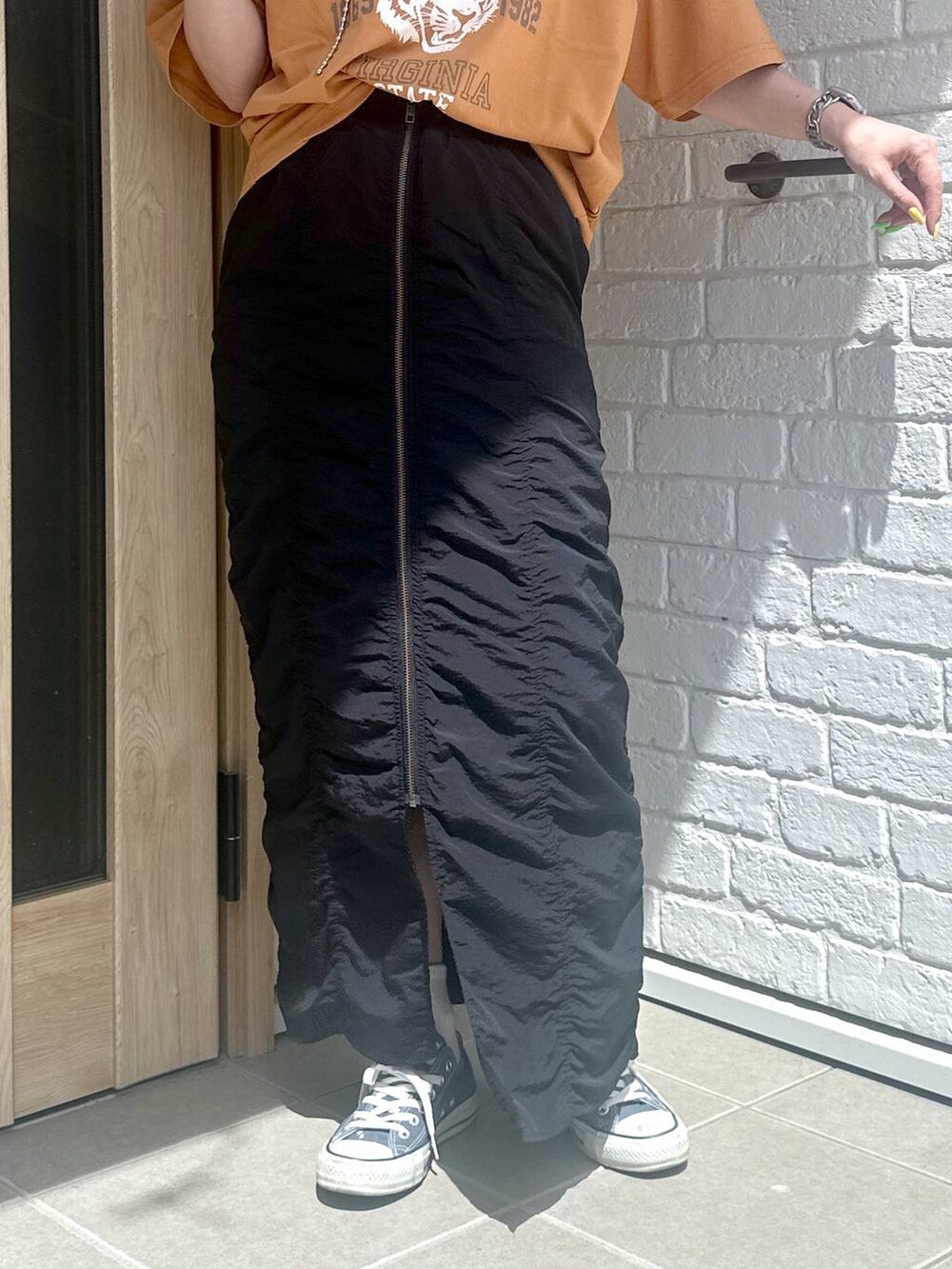 ブラック系のスカート、オレンジ系のTシャツ/カットソー、シルバー系のデジタル腕時計を着用したレディースの春コーディネートの4枚目の写真