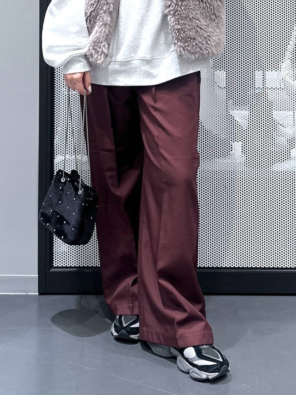 グレー系のベスト、ブラック系のショルダーバッグ、レッド系のスラックスを着用したレディースの秋コーディネートの5枚目の写真