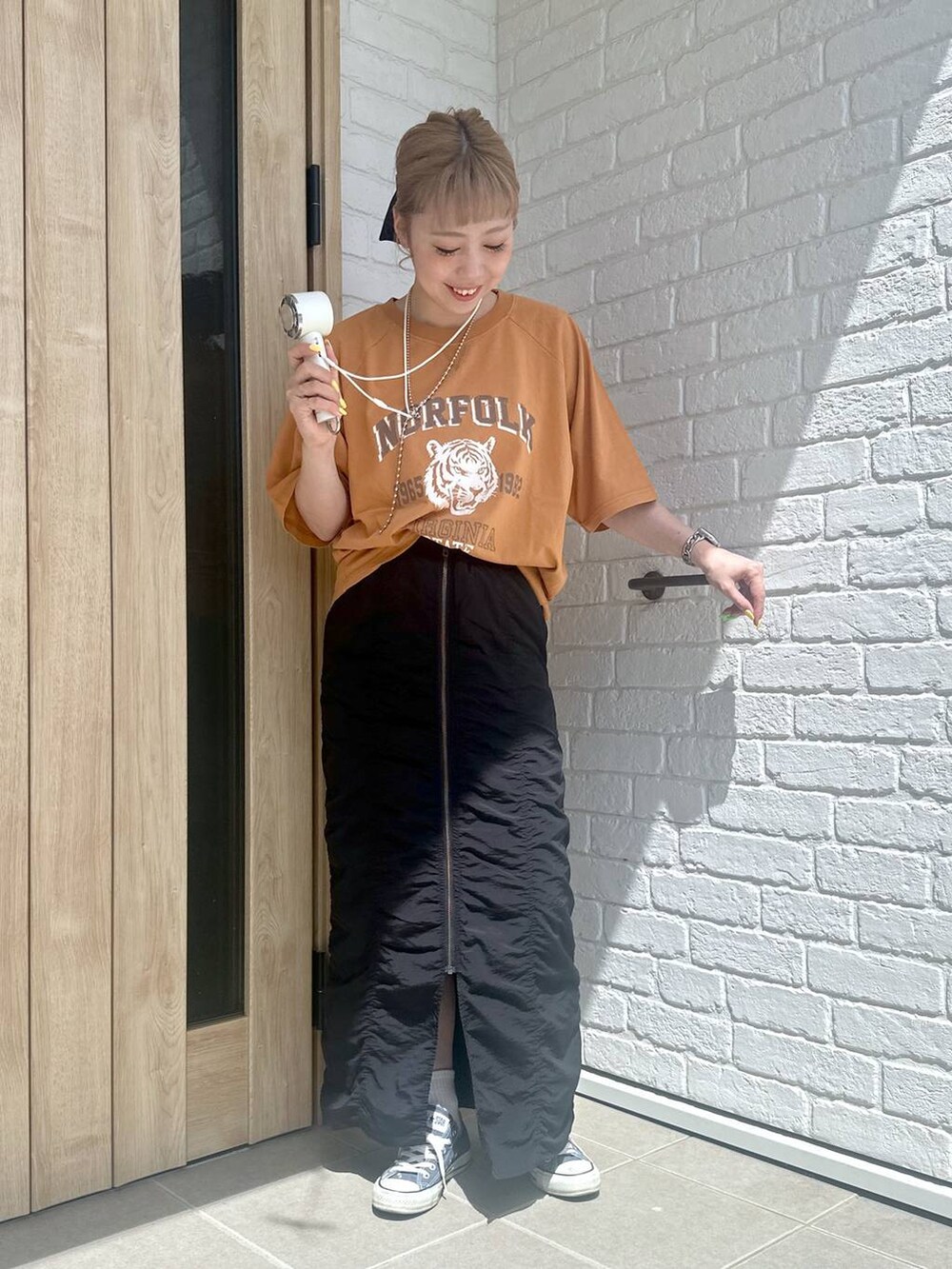 ブラック系のスカート、オレンジ系のTシャツ/カットソー、シルバー系のデジタル腕時計を着用したレディースの春コーディネートの5枚目の写真