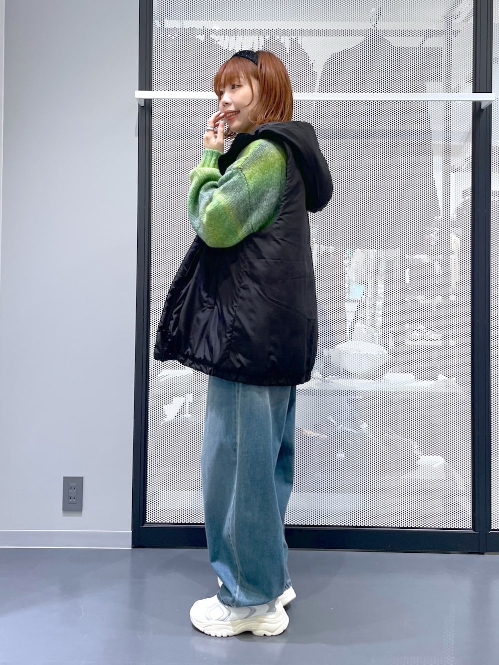 ブルー系のデニムパンツ、ホワイト系のスニーカー、ブラック系のベストを着用したレディースの秋コーディネートの2枚目の写真