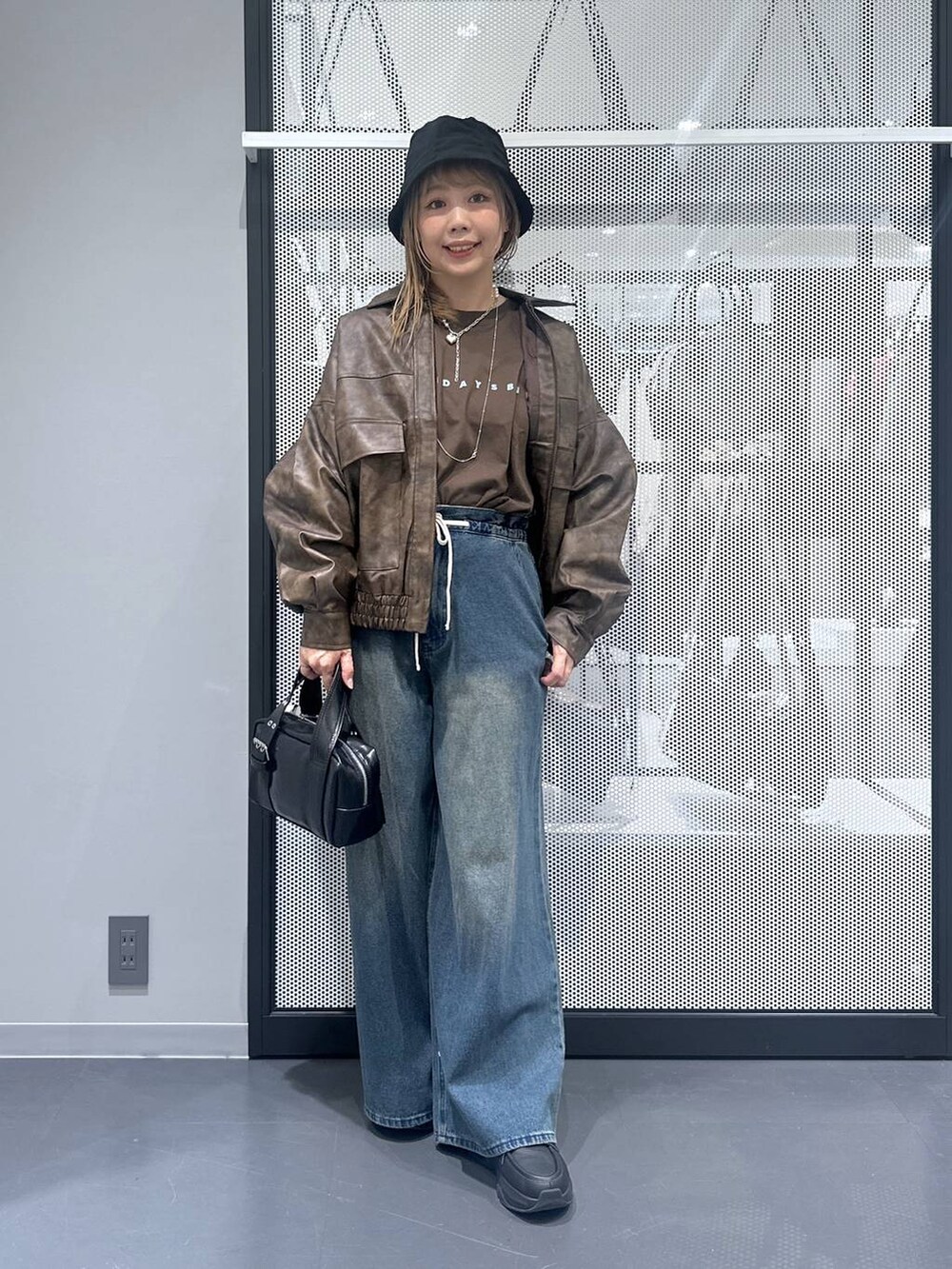 ブラウン系のブルゾン、ブラック系のショルダーバッグ、ブルー系のデニムパンツを着用したレディースの秋コーディネートの2枚目の写真