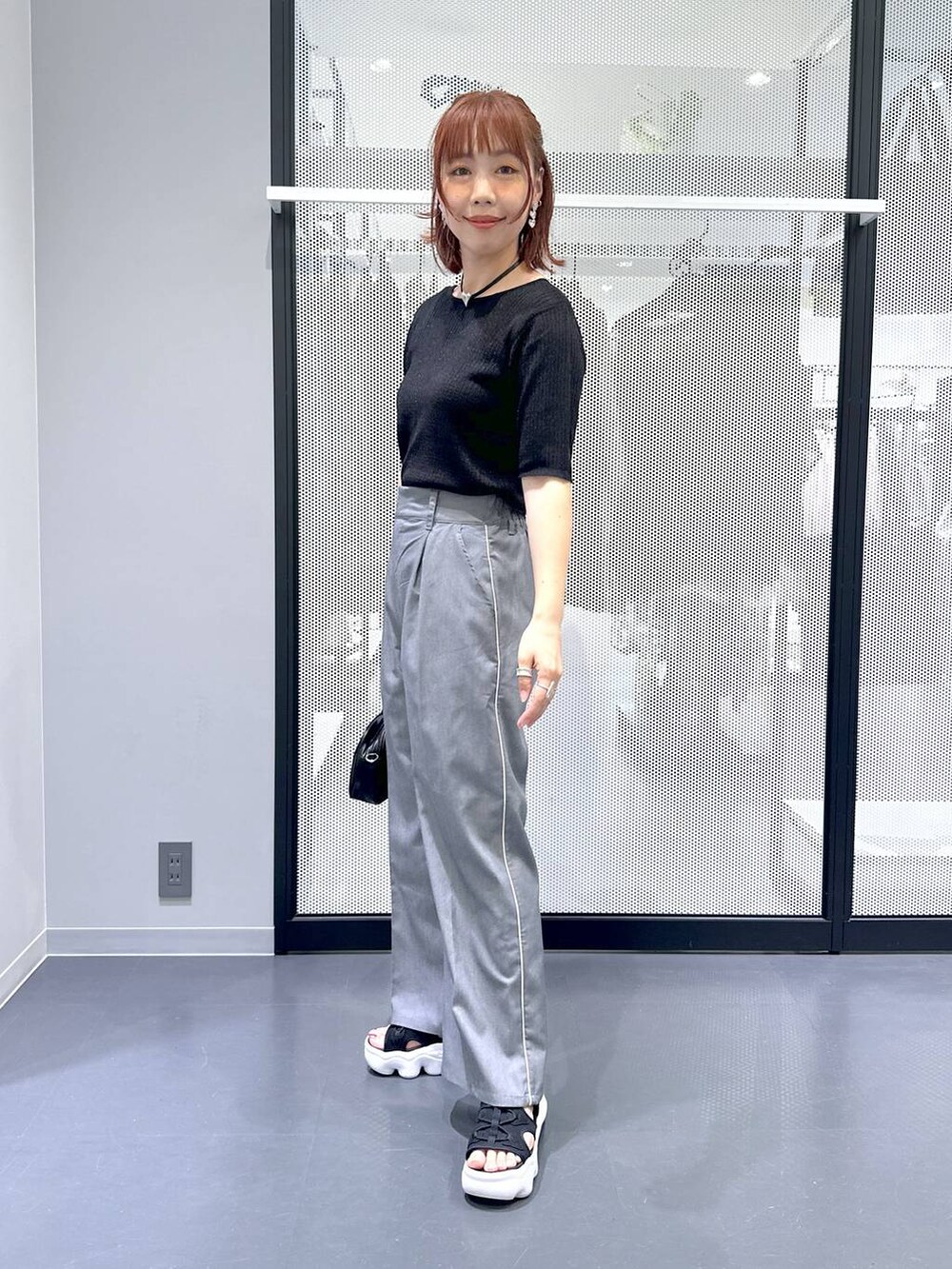 ブラック系のショルダーバッグ、ブラック系のカーディガン/ボレロ、グレー系のスラックスを着用したレディースの夏コーディネートの5枚目の写真