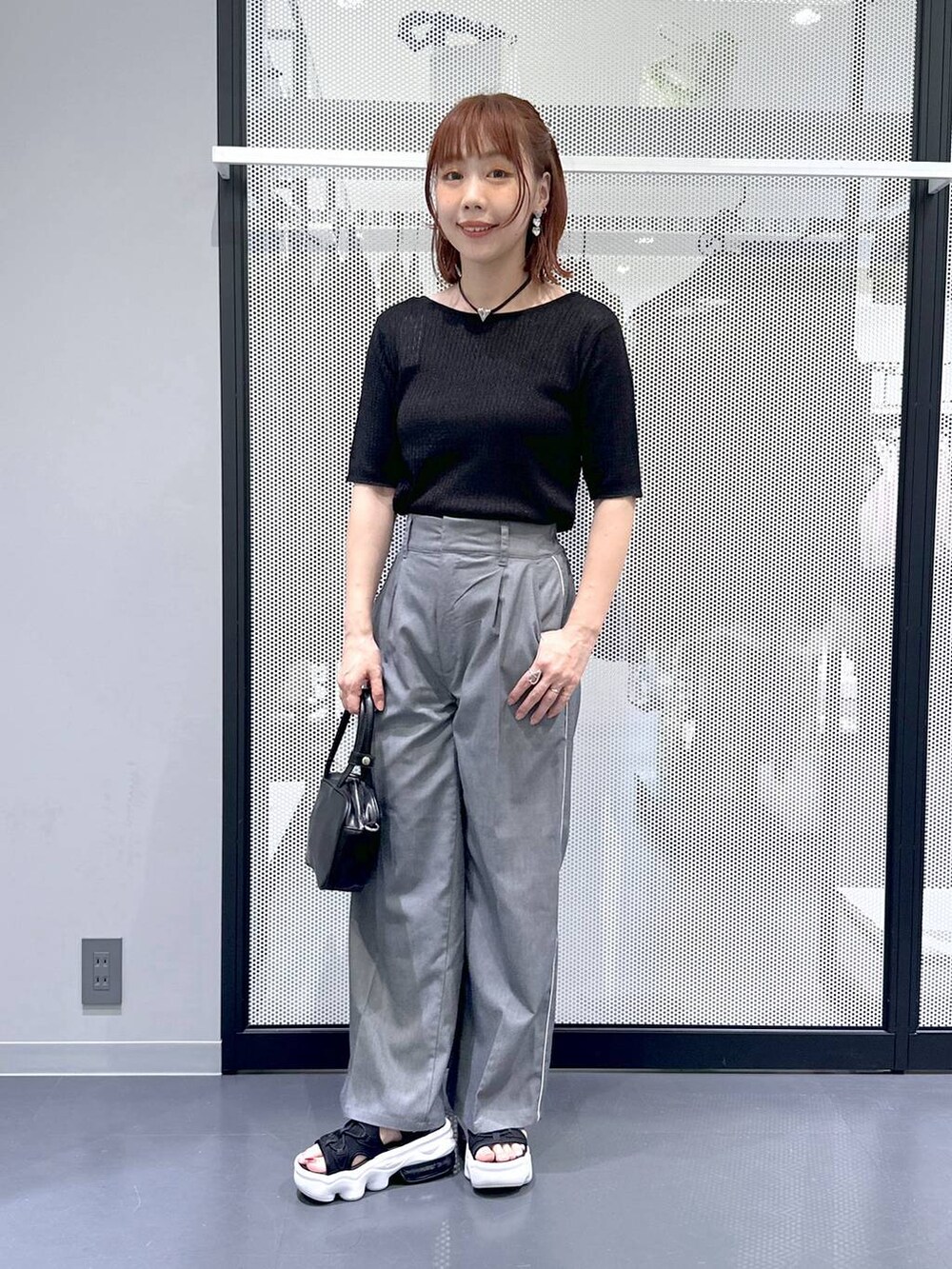 ブラック系のショルダーバッグ、ブラック系のカーディガン/ボレロ、グレー系のスラックスを着用したレディースの夏コーディネートの2枚目の写真