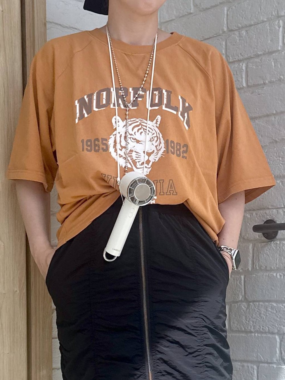 ブラック系のスカート、オレンジ系のTシャツ/カットソー、シルバー系のデジタル腕時計を着用したレディースの春コーディネートの3枚目の写真