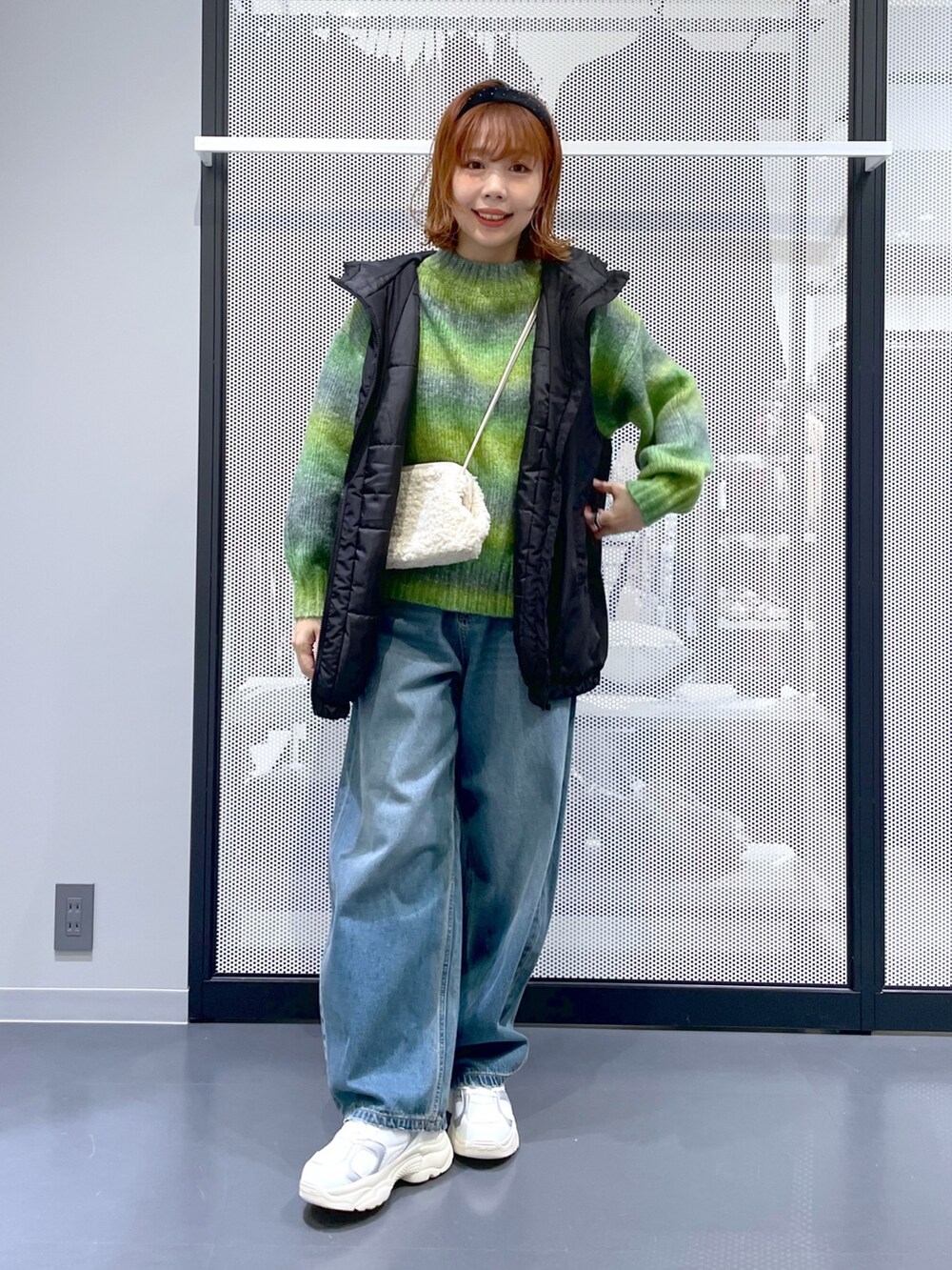 ブルー系のデニムパンツ、ホワイト系のスニーカー、ブラック系のベストを着用したレディースの秋コーディネートの3枚目の写真