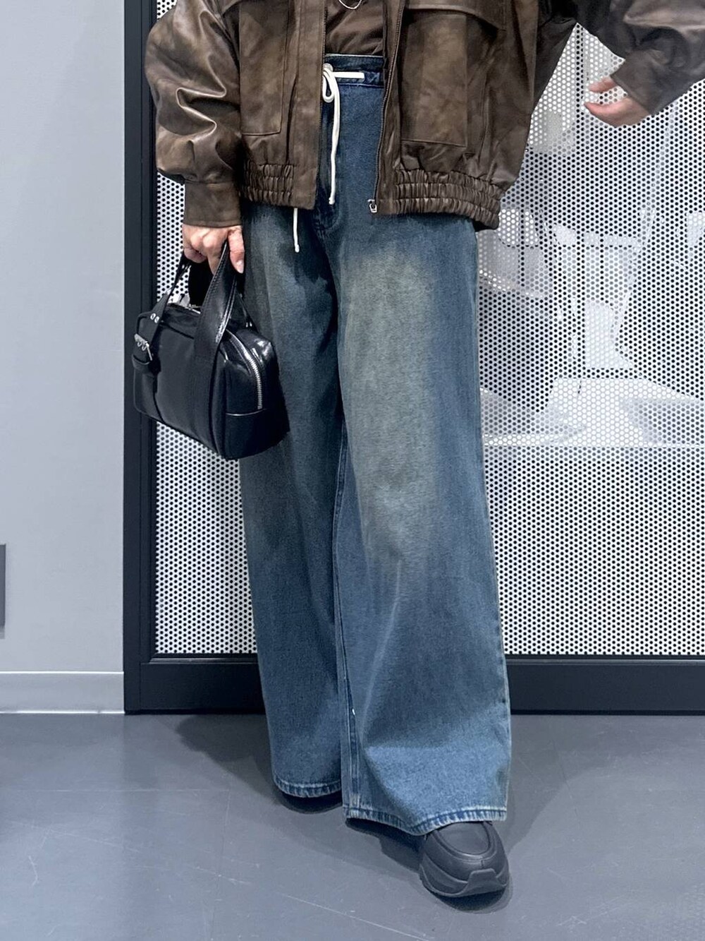 ブラウン系のブルゾン、ブラック系のショルダーバッグ、ブルー系のデニムパンツを着用したレディースの秋コーディネートの5枚目の写真