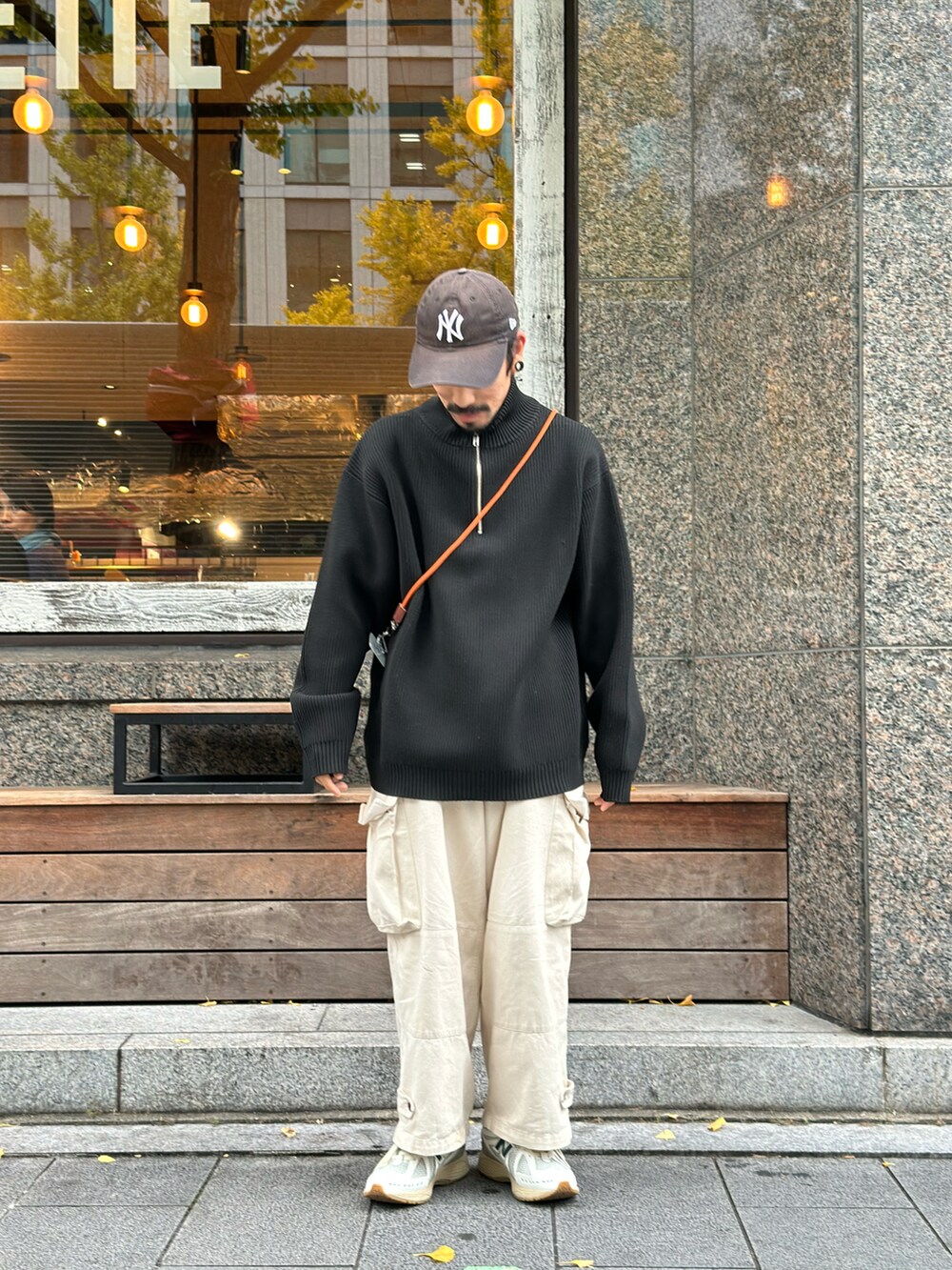 ブラック系のニット/セーター、オレンジ系のスマホグッズを着用したメンズの秋コーディネートの2枚目の写真