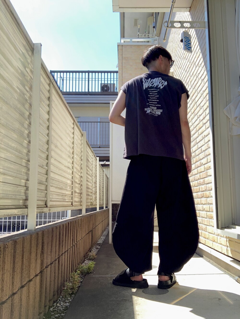 ブラック系のTシャツ/カットソー、ブラック系のスラックス、ブラック系のサンダルを着用したメンズの夏コーディネートの2枚目の写真