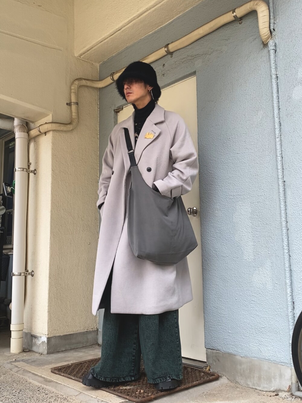 グレー系のショルダーバッグ、グレー系のチェスターコート、ブラック系のニット/セーターを着用したメンズの冬コーディネートの2枚目の写真