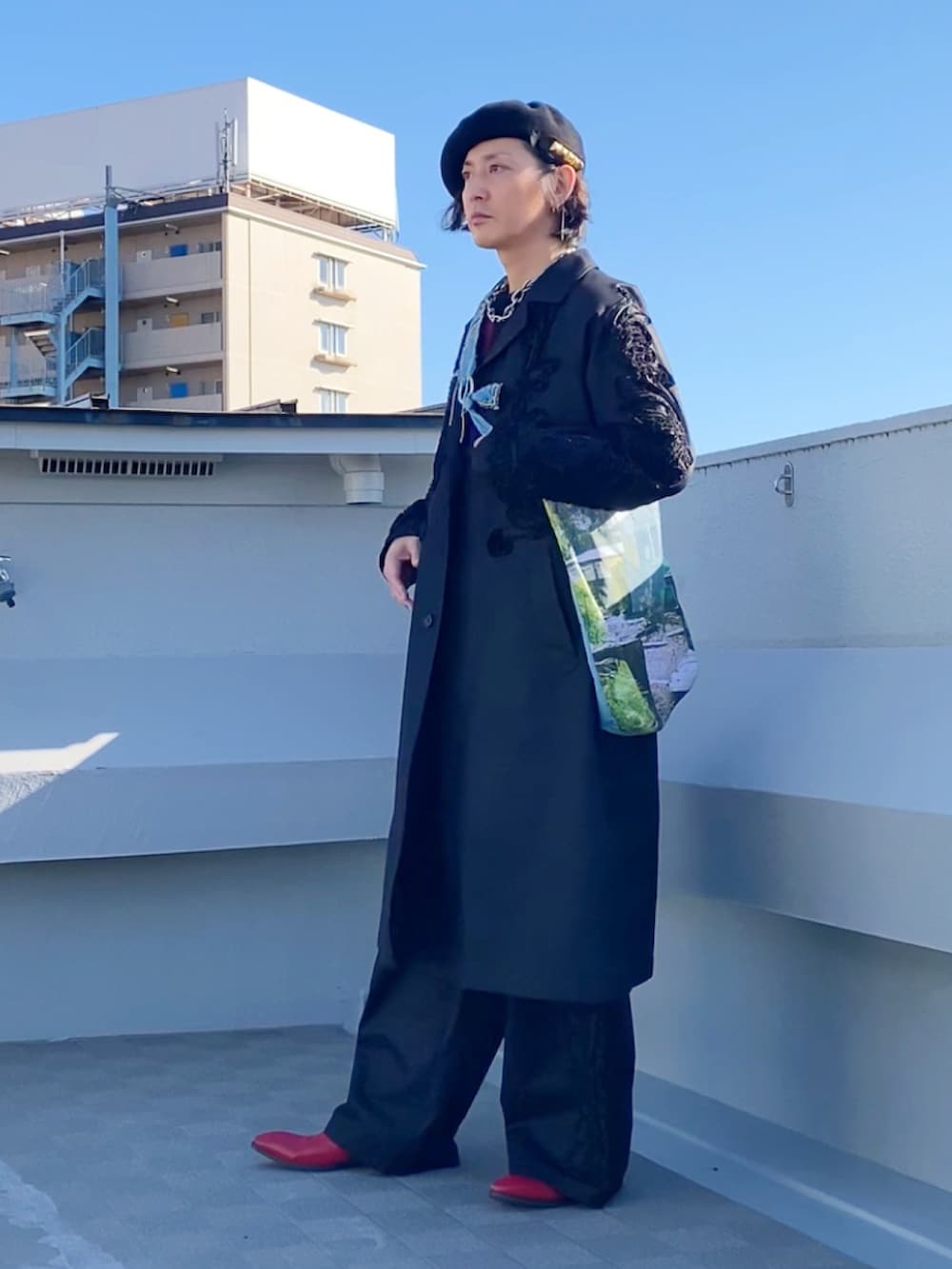 レッド系のニット/セーター、ブラック系のステンカラーコート、ブラック系のパンツを着用したメンズの冬コーディネートの2枚目の写真