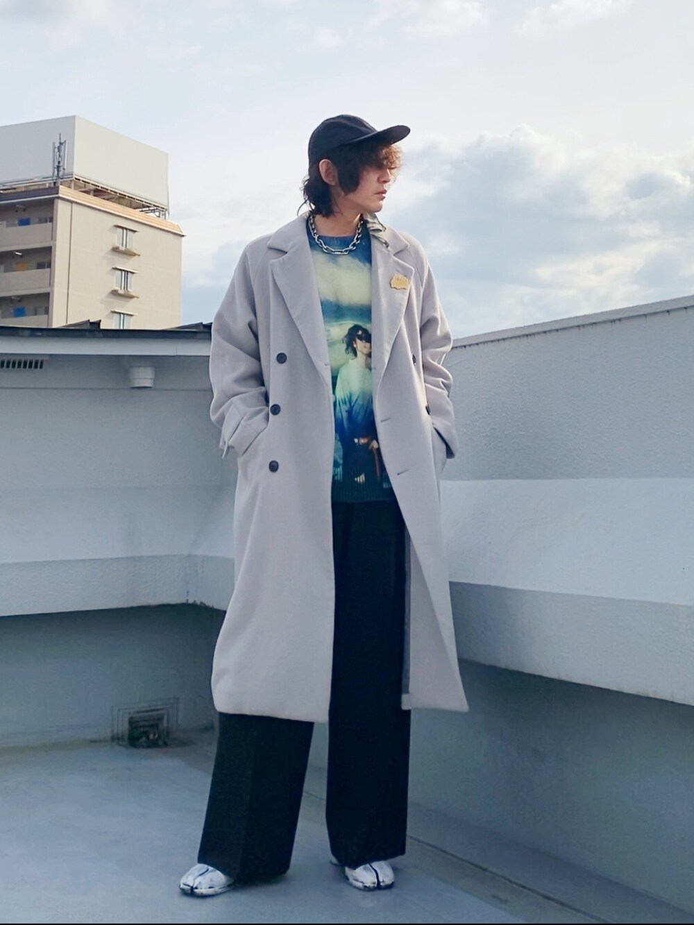 グレー系のチェスターコート、ブルー系のニット/セーター、ブラック系のスラックスを着用したメンズの冬コーディネートの2枚目の写真