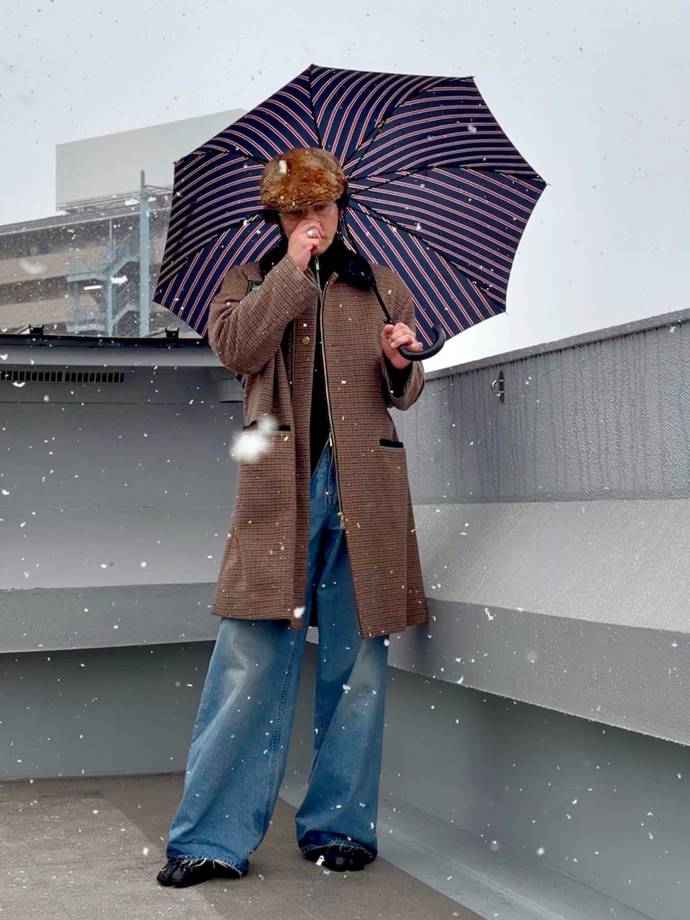 ブラック系のニット/セーター、ブラウン系のステンカラーコート、ブルー系のデニムパンツを着用したメンズの冬コーディネートの2枚目の写真