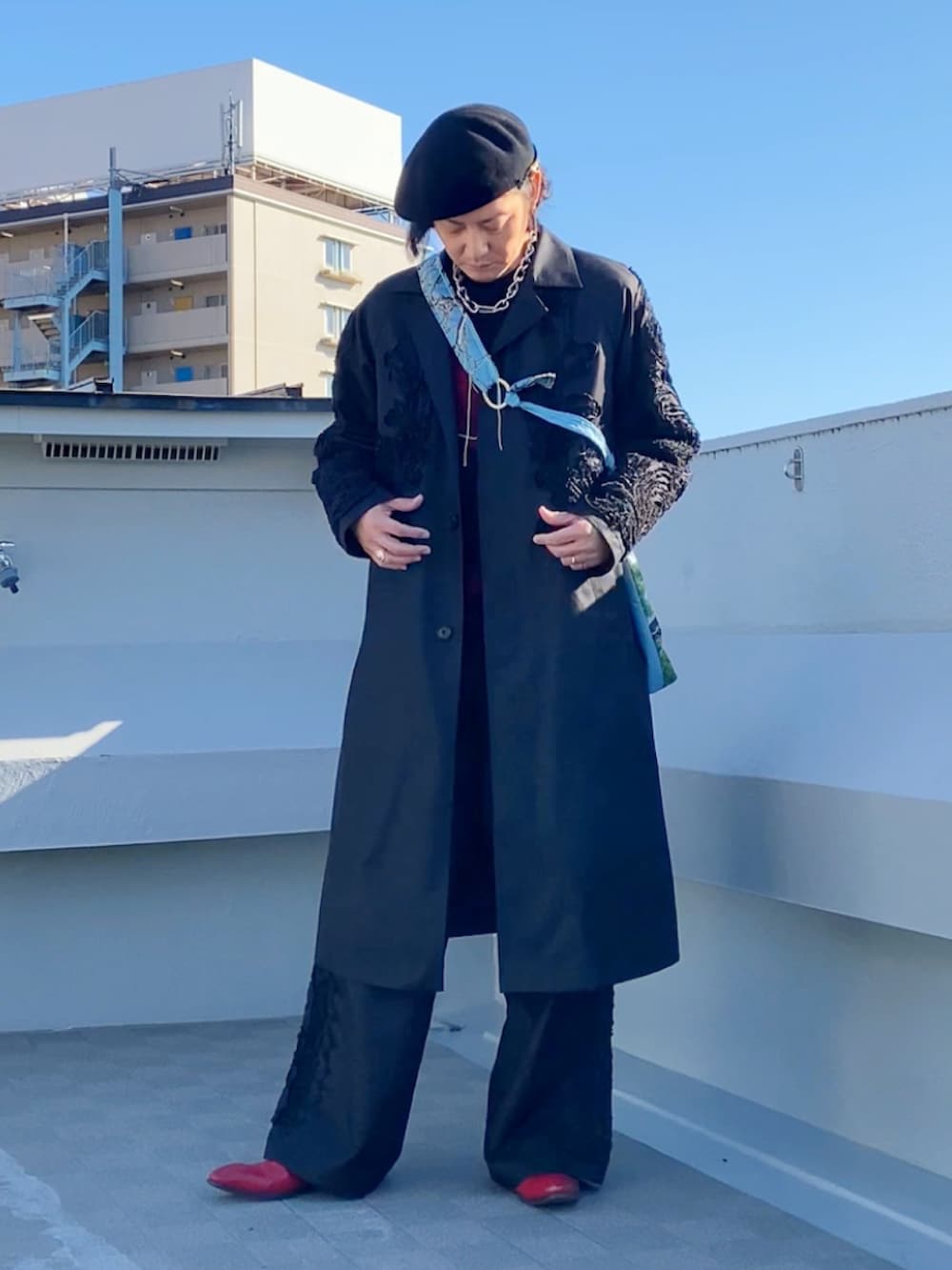 レッド系のニット/セーター、ブラック系のステンカラーコート、ブラック系のパンツを着用したメンズの冬コーディネートの5枚目の写真