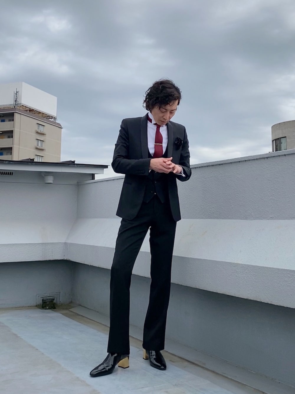 ブラック系のテーラードジャケット、ブラック系のブーツ、ブラック系のスラックスを着用したメンズの春コーディネートの2枚目の写真