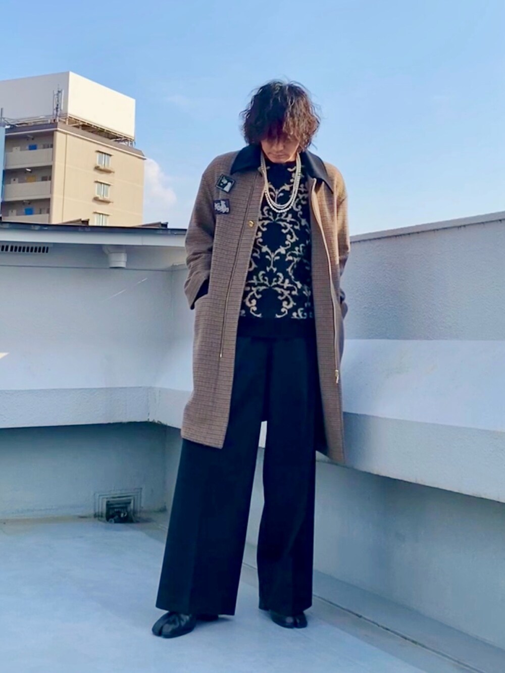 ブラウン系のステンカラーコート、ブラック系のニット/セーター、ブラック系のスラックスを着用したメンズの冬コーディネートの2枚目の写真