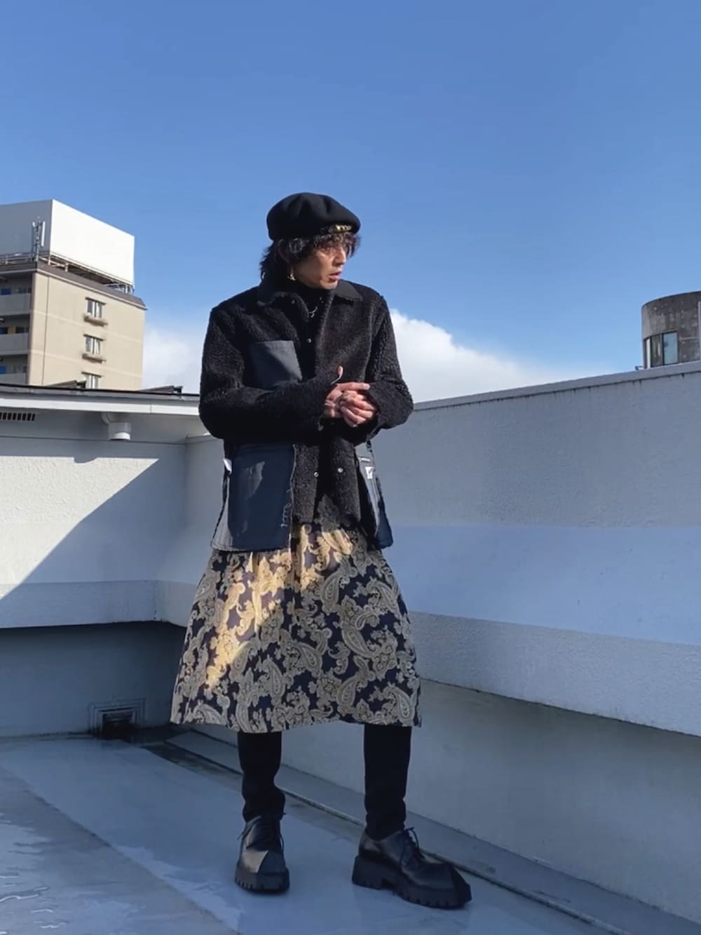 ブラック系のムートンコート、ブルー系のスカート、ブラック系のドレスシューズを着用したメンズの春コーディネートの4枚目の写真