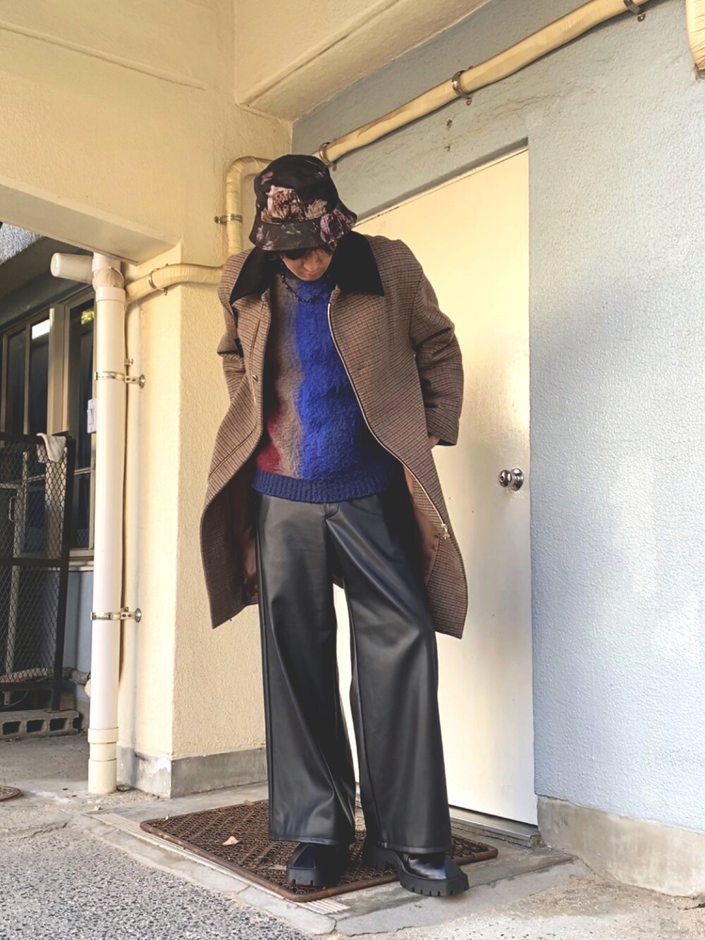 ブラウン系のステンカラーコート、ブルー系のニット/セーター、ブラック系のその他パンツを着用したメンズの冬コーディネートの2枚目の写真