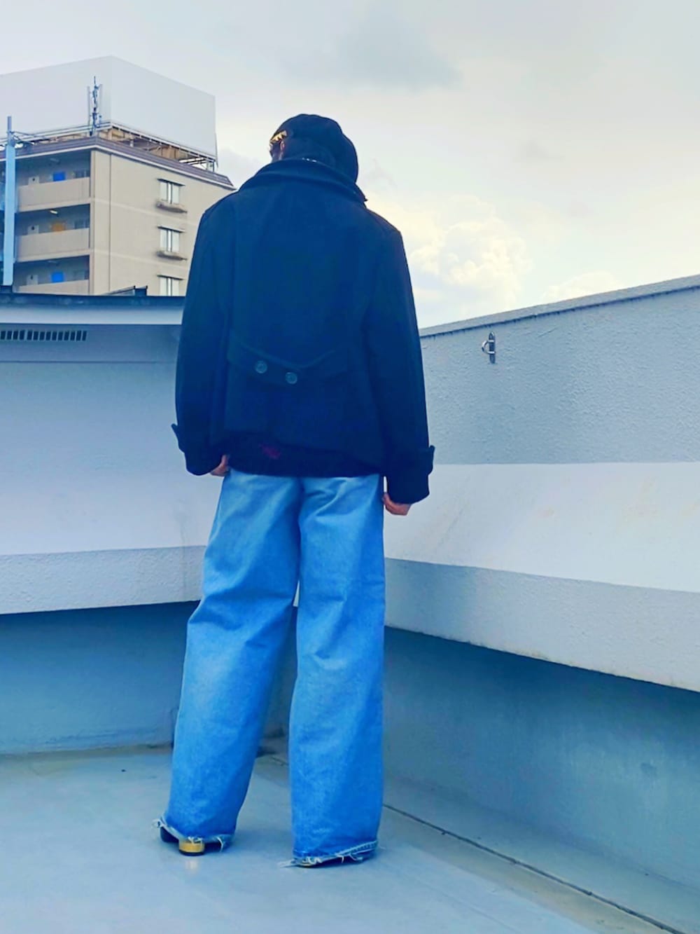 ブラック系のピーコート、レッド系のニット/セーター、ブルー系のデニムパンツを着用したメンズの冬コーディネートの4枚目の写真