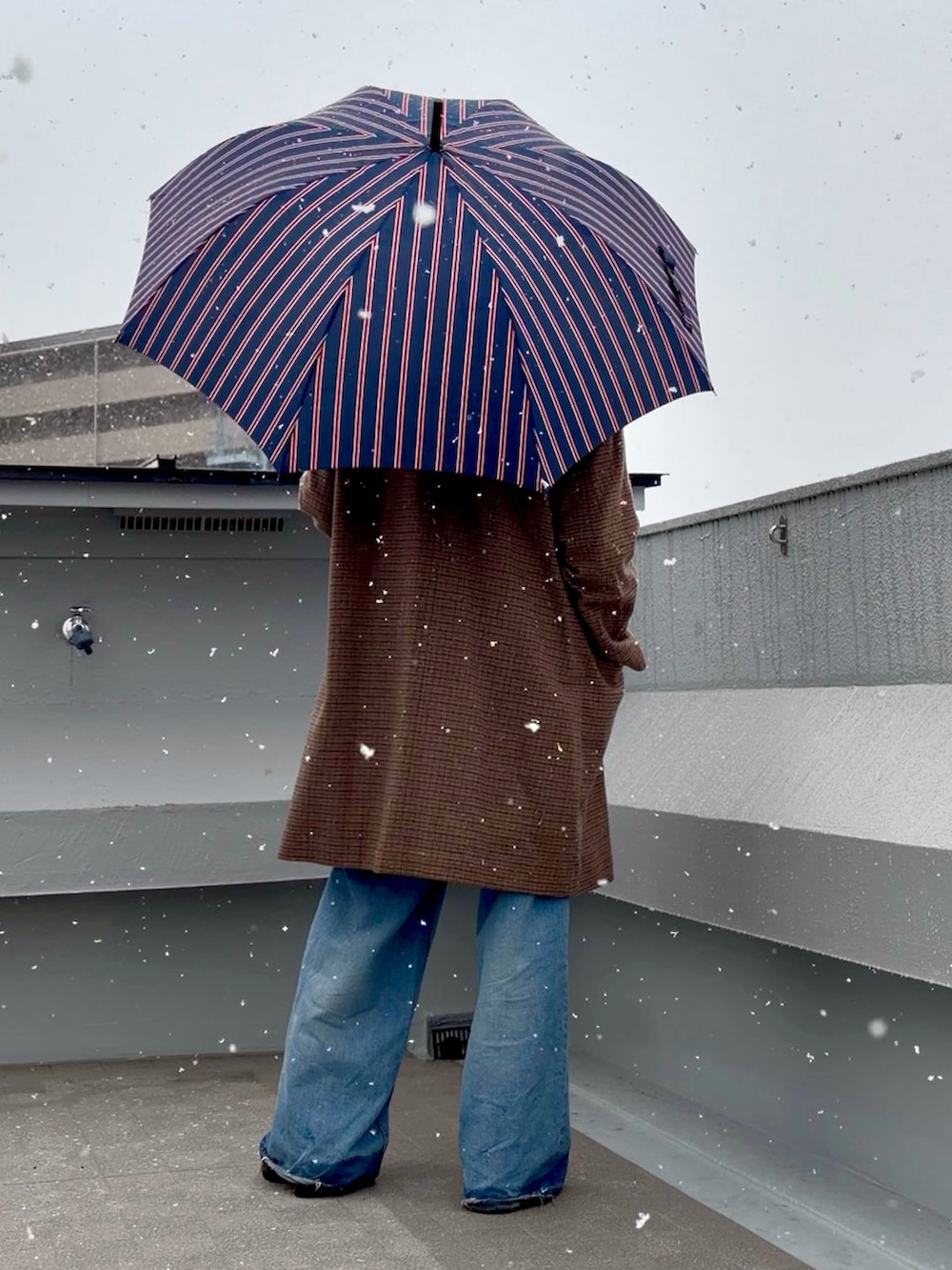 ブラック系のニット/セーター、ブラウン系のステンカラーコート、ブルー系のデニムパンツを着用したメンズの冬コーディネートの4枚目の写真