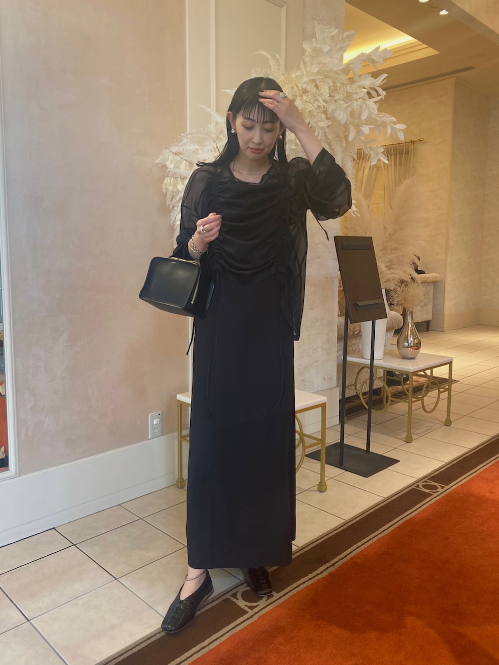 ブラック系のワンピース、ブラック系のパンプス、シルバー系のイヤリングを着用したレディースの春コーディネートの2枚目の写真