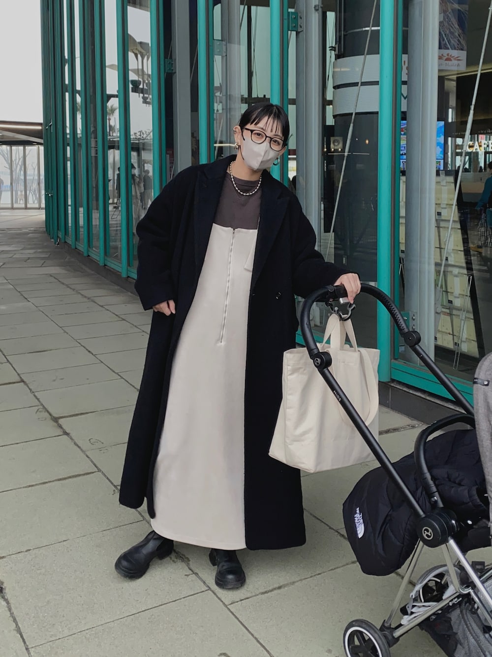 ホワイト系のジャンパースカート、ブラック系のチェスターコート、ブラック系のブーツを着用したレディースの冬コーディネートの2枚目の写真