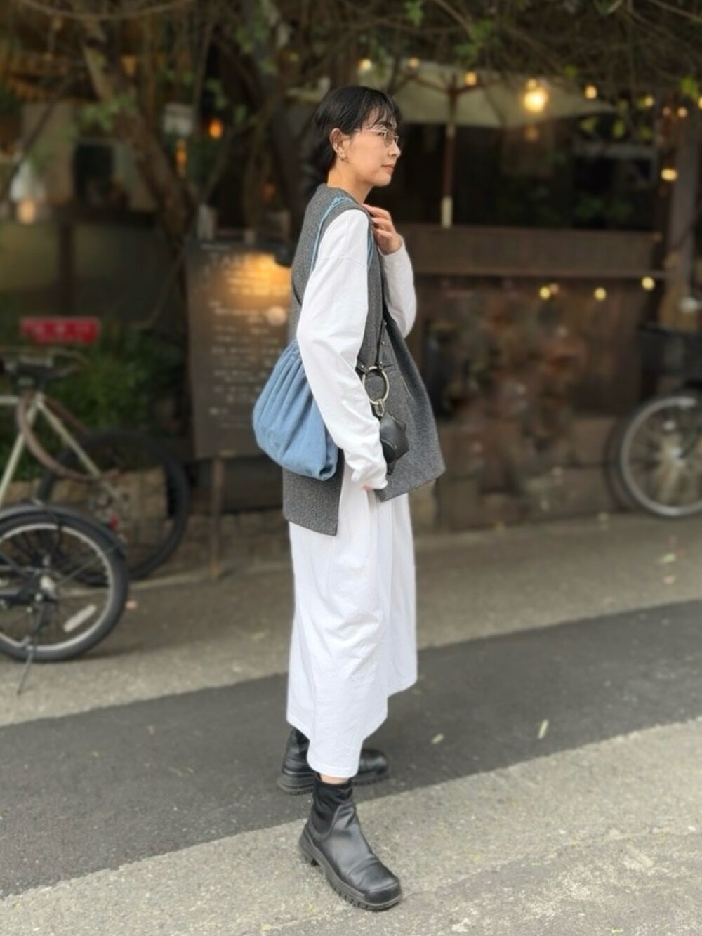 グレー系のベスト、ブラック系のショルダーバッグ、ブラック系のブーツを着用したレディースの秋コーディネートの4枚目の写真