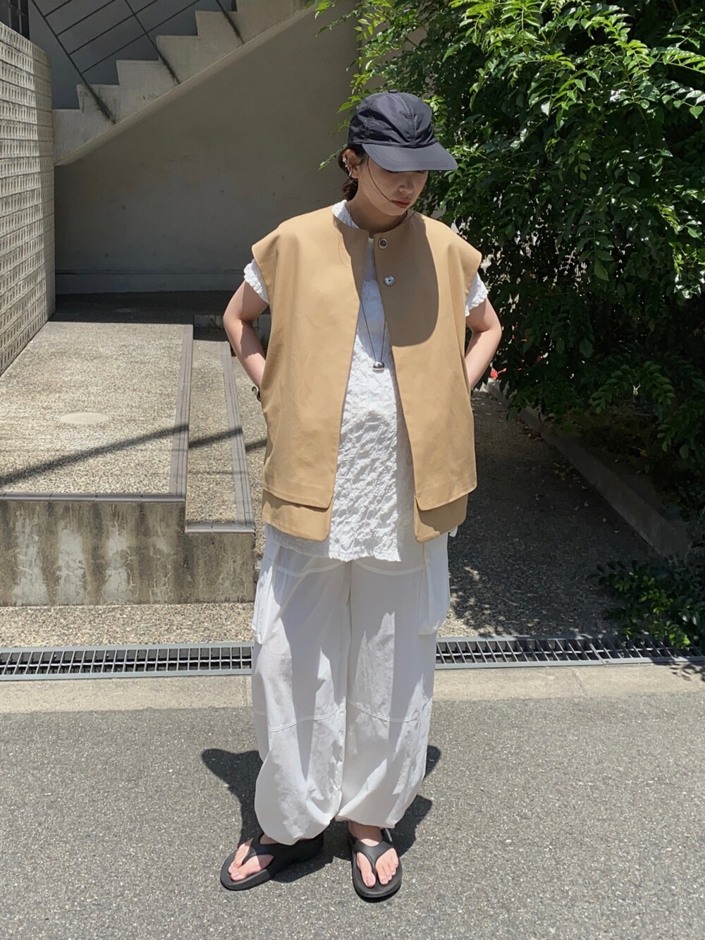 ベージュ系のベスト、ブラック系のサンダル、ブラック系のキャップを着用したレディースの秋コーディネートの2枚目の写真